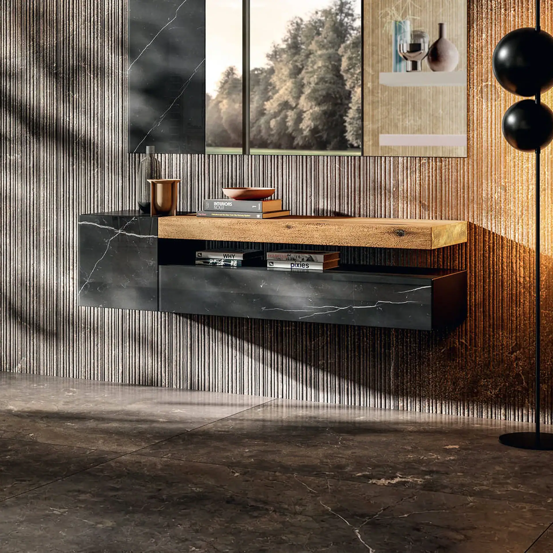 A modern floating media console made of dark veined marble and light wood, set against a textured, grooved wall. Books and decorative items adorn the console, with a large mirror reflecting trees above it. A black floor lamp stands to the right.