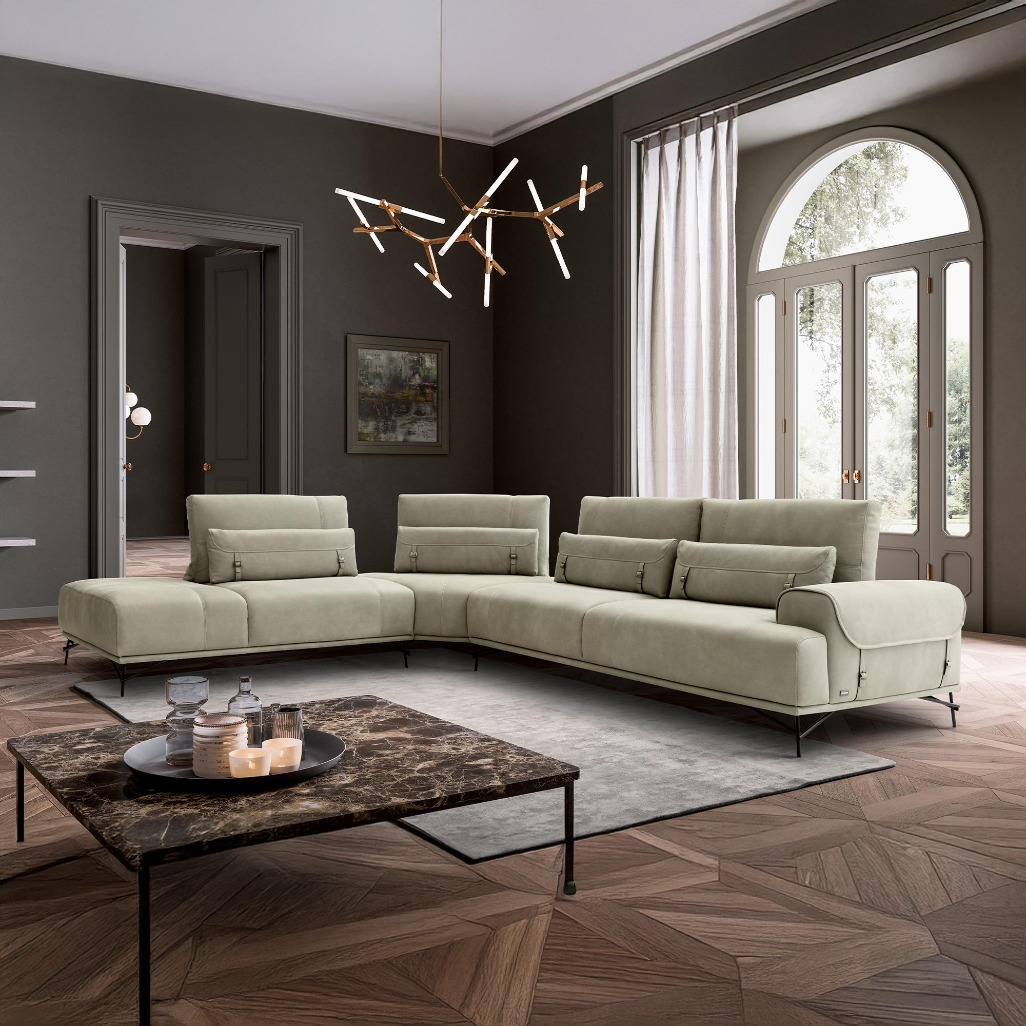 A modern living room with a light beige L-shaped sectional sofa, a dark marble coffee table, and a unique branching chandelier, set against dark gray walls and a parquet floor, with an arched window overlooking trees.