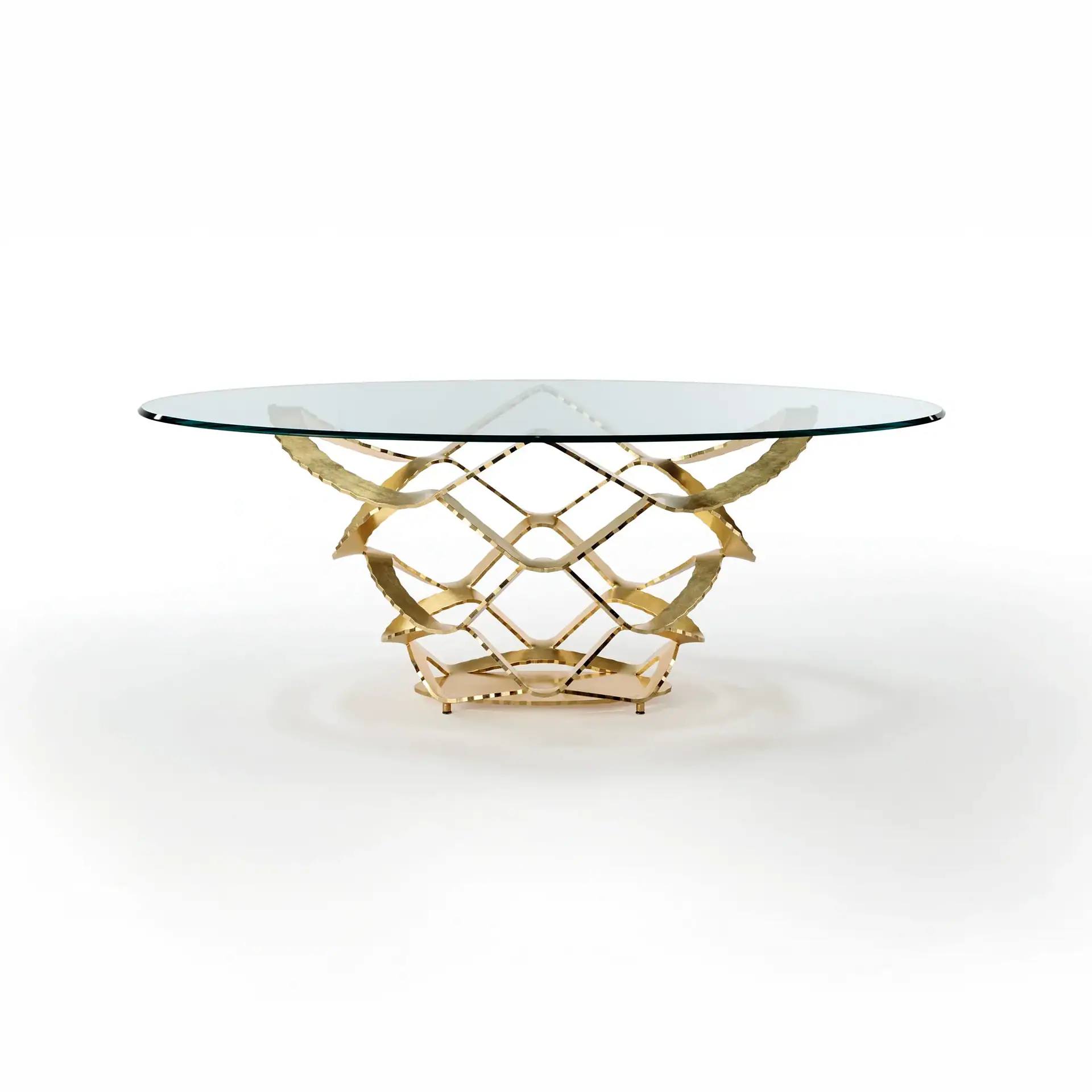 A round table with a clear glass top and an ornate, gold-colored metal base with a wavy, lattice-like design on a white background.