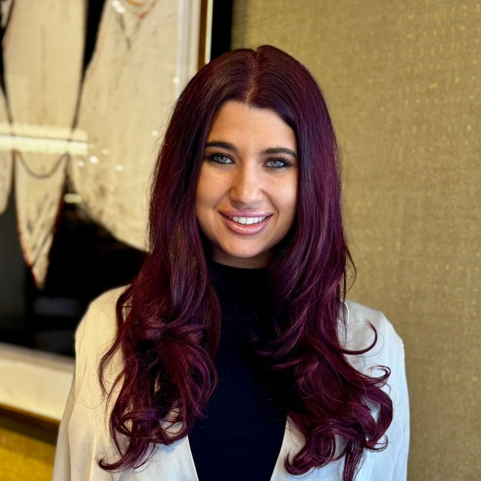 Elegant woman with long, wavy burgundy hair smiling indoors.