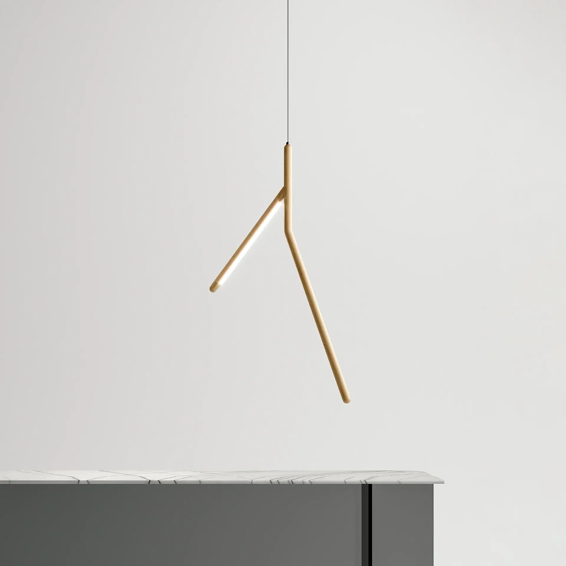 A modern Y-shaped wooden pendant light with an illuminated LED strip hangs above a dark grey counter with a white marble top, against a light grey wall.