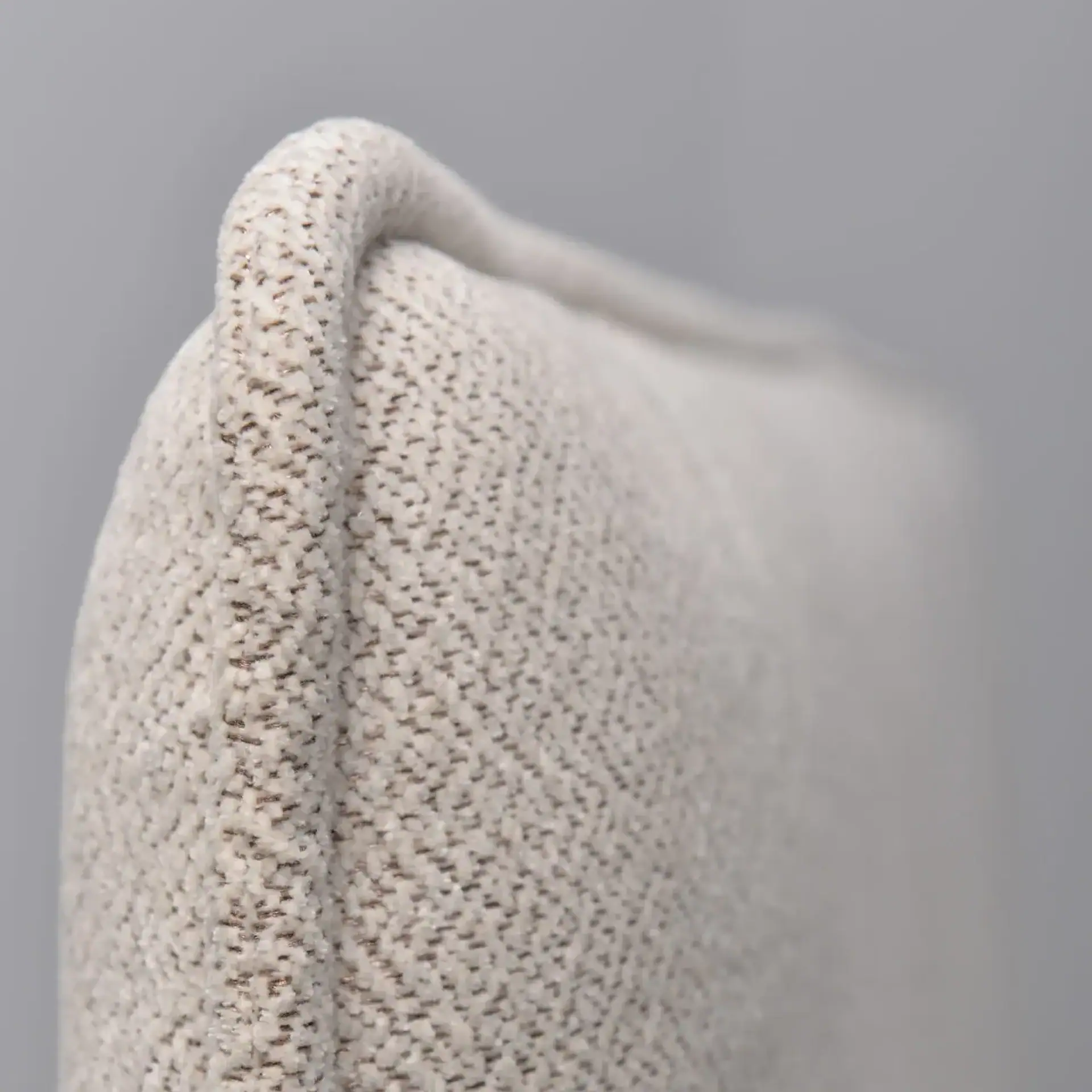 Close-up of a light cream-colored, textured fabric with a subtle woven pattern and a rounded edge against a gray background.