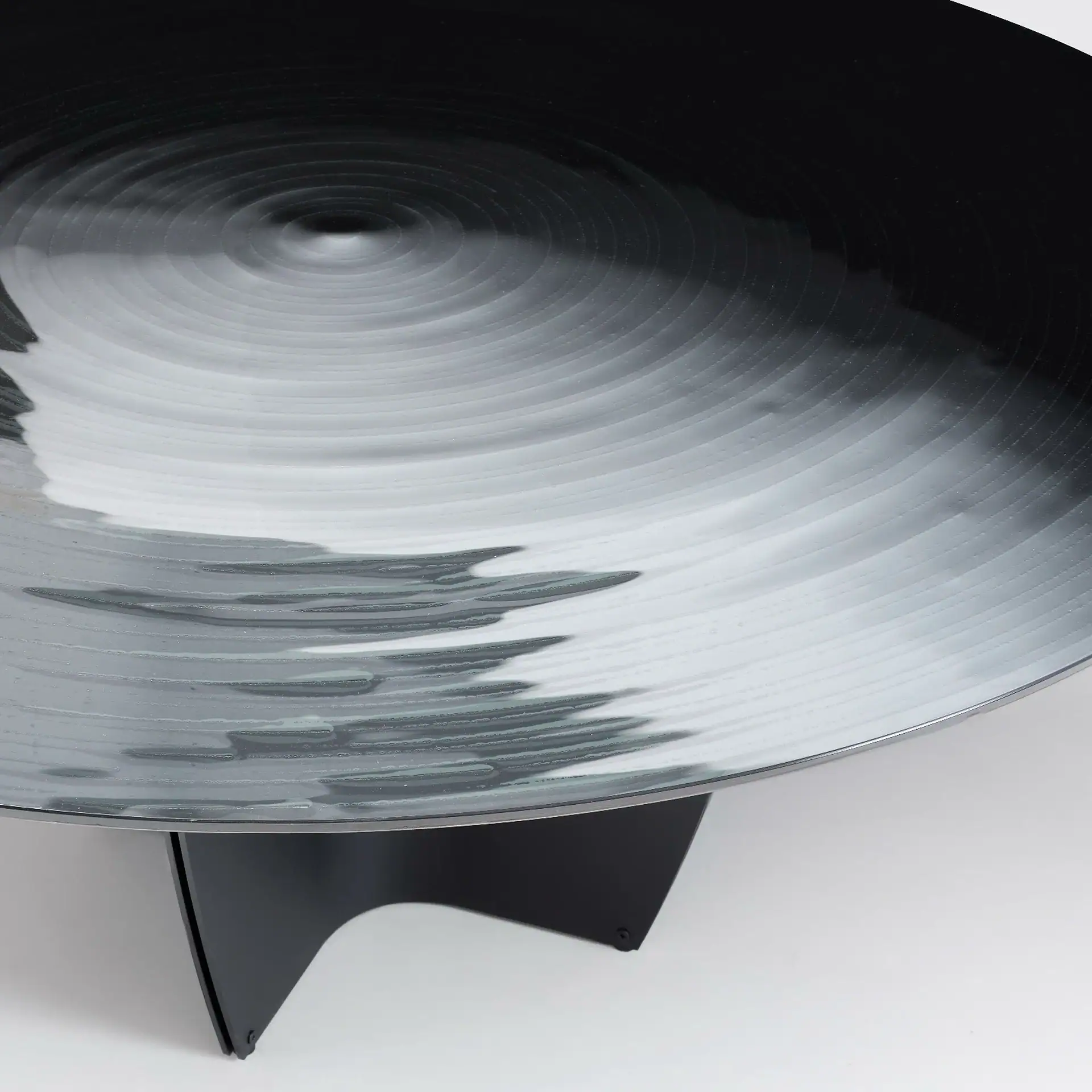 A large, dark, round object with concentric ripple patterns on its surface, supported by a black, angular base against a light background.