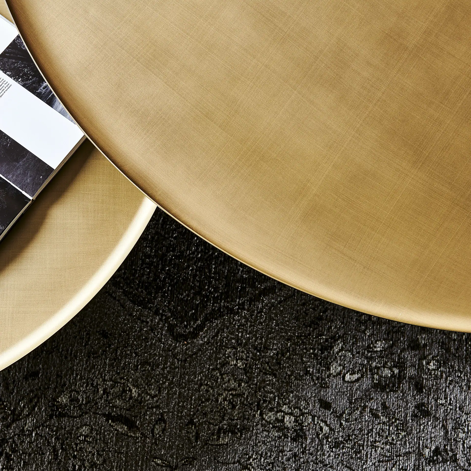 Overhead view of brushed gold surfaces, a textured dark gray surface, and a black and white patterned book.
