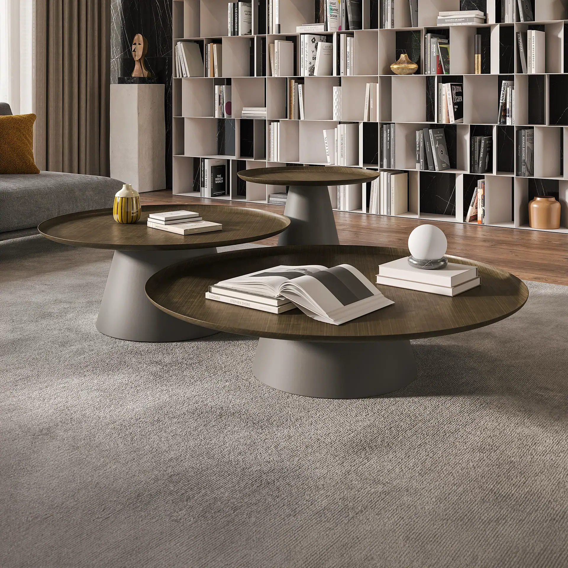 A modern living room with three round coffee tables, a gray sofa, and a large white bookcase filled with books and decorative items.