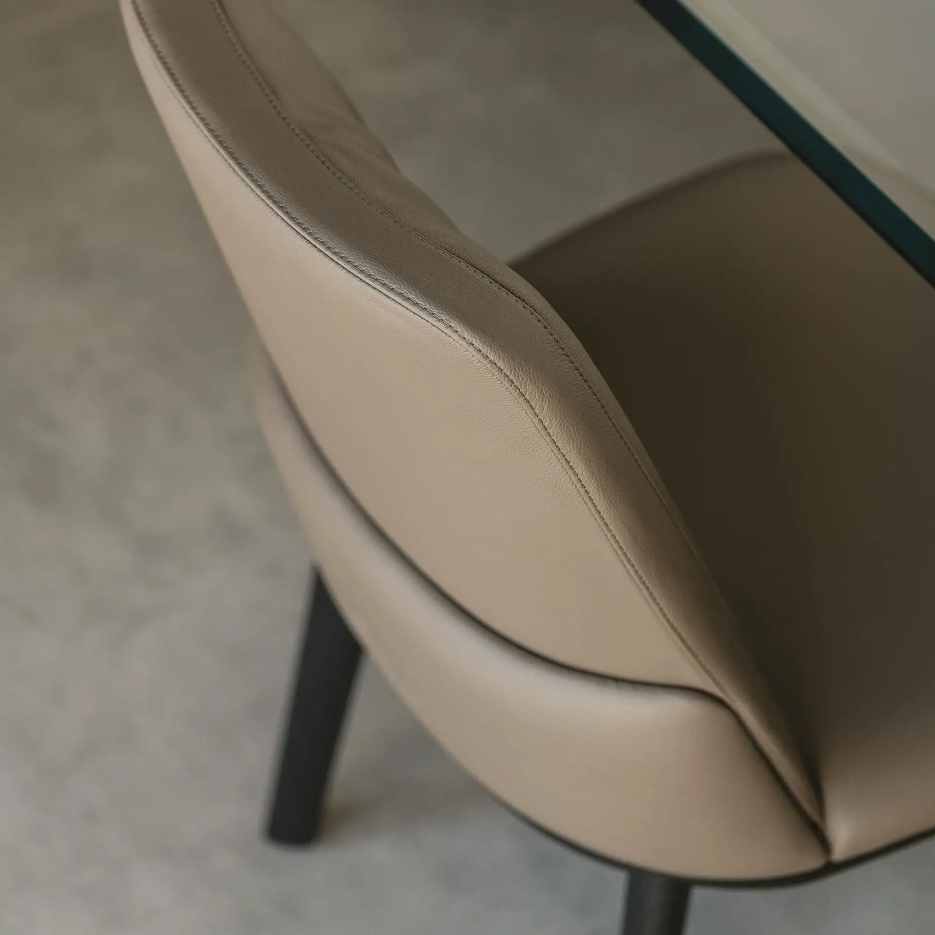 Close-up of a light beige leather chair with visible stitching, a dark leg, and a glass table edge in the background.