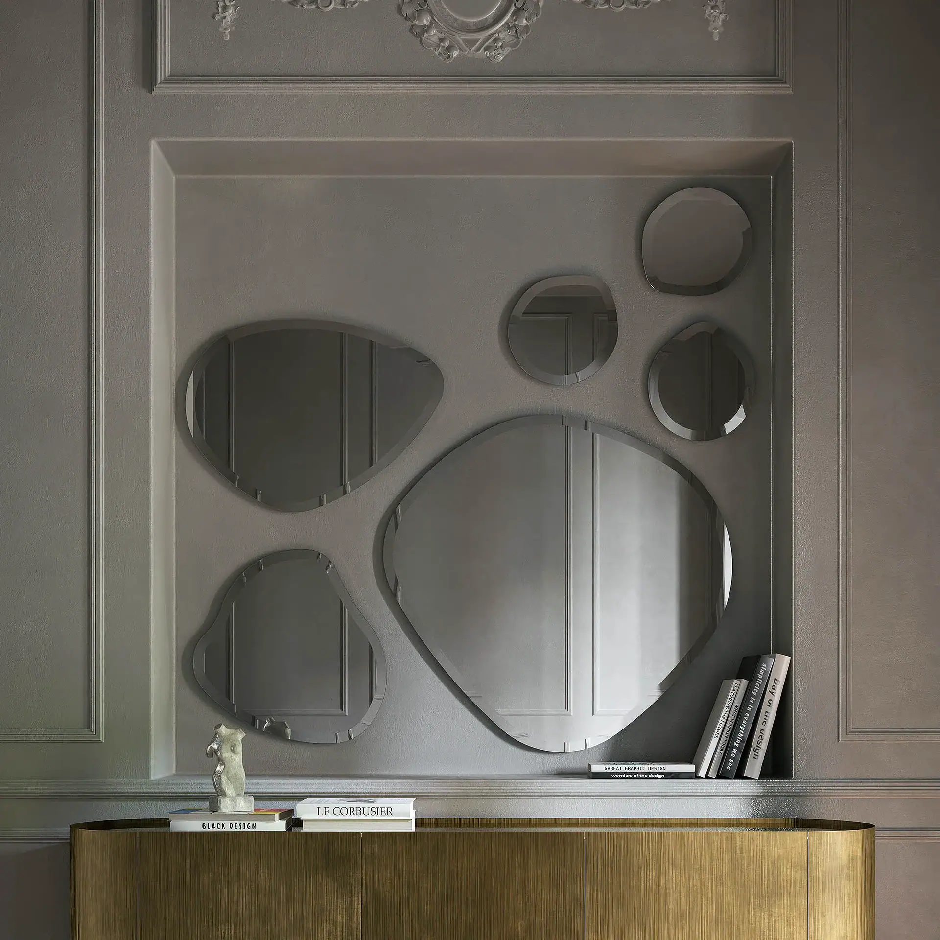 A gray wall with classical molding and a recessed niche containing five irregularly shaped mirrors. Below, a golden console table holds a white torso sculpture and books.
