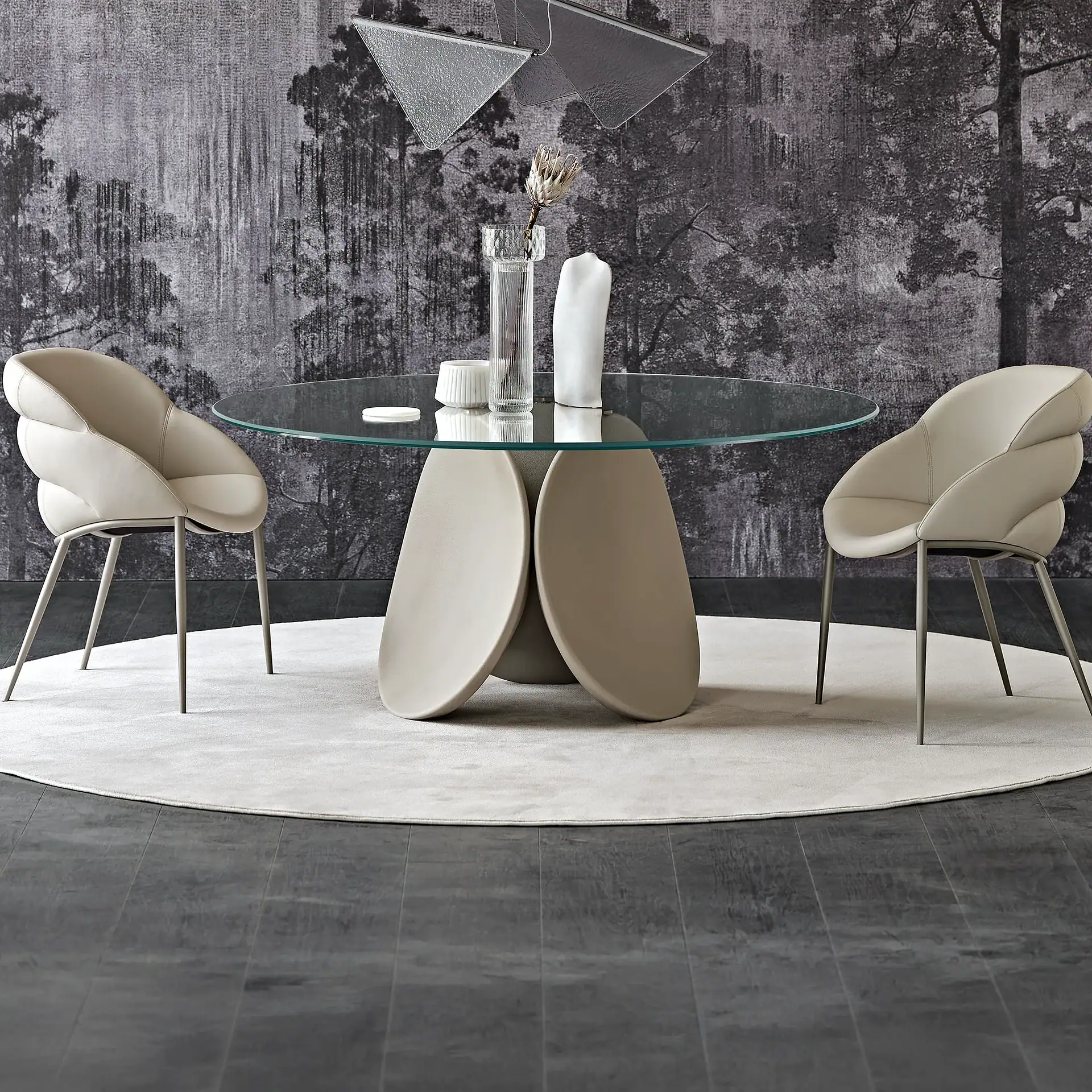 A modern dining room with a round glass table, two cream upholstered chairs, a light rug, and dark wood floors against a forest-patterned wallpaper.