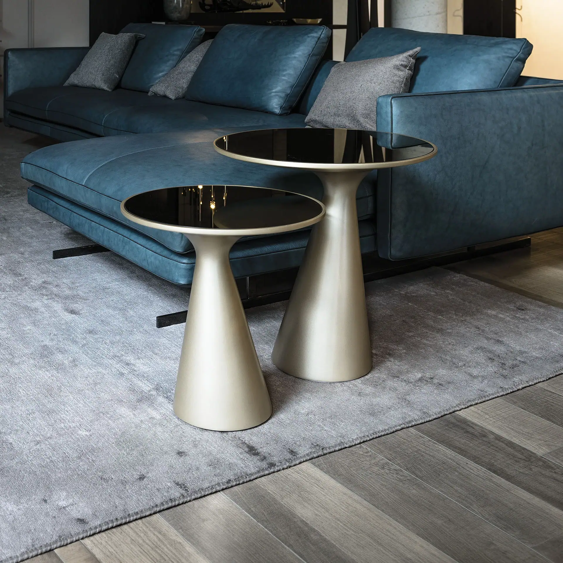Sklar Furnishings end tables with black tops and metallic bases in front of a blue sofa.