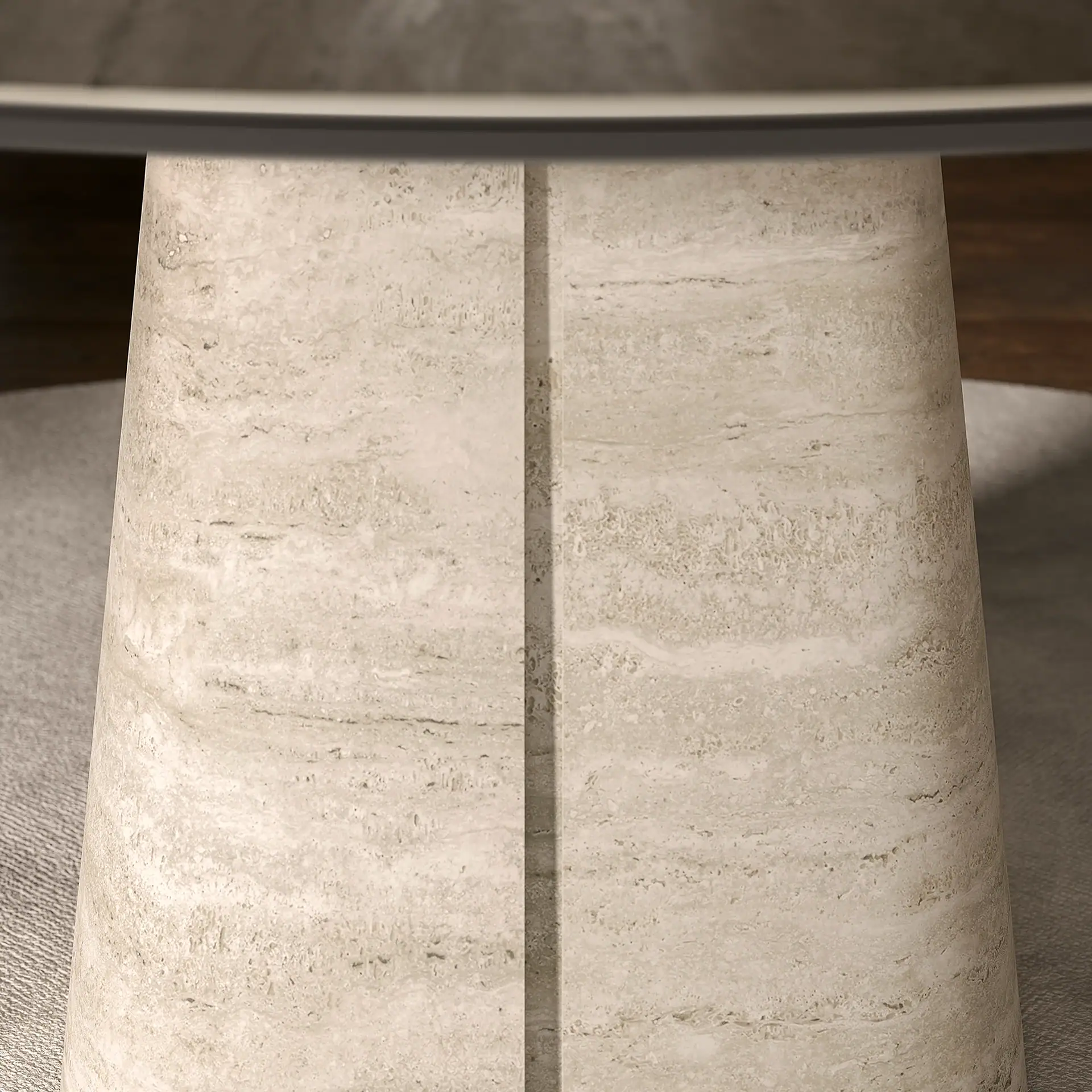 Close-up of a cylindrical travertine table base with a vertical groove, supporting a glass tabletop, on a gray rug.
