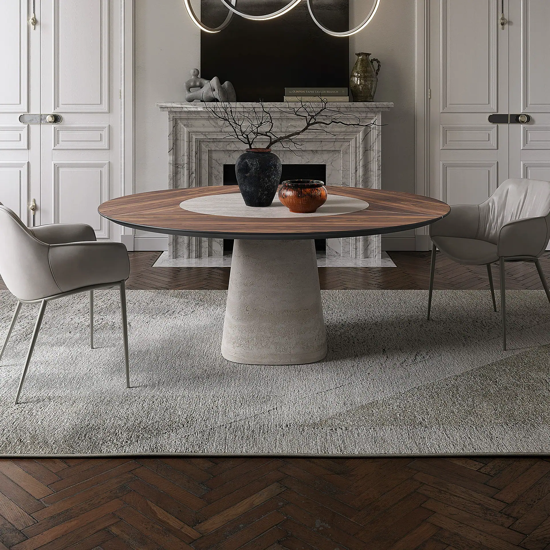 A modern dining room with a round wooden table on a conical base, two gray chairs, and a marble fireplace with decor.