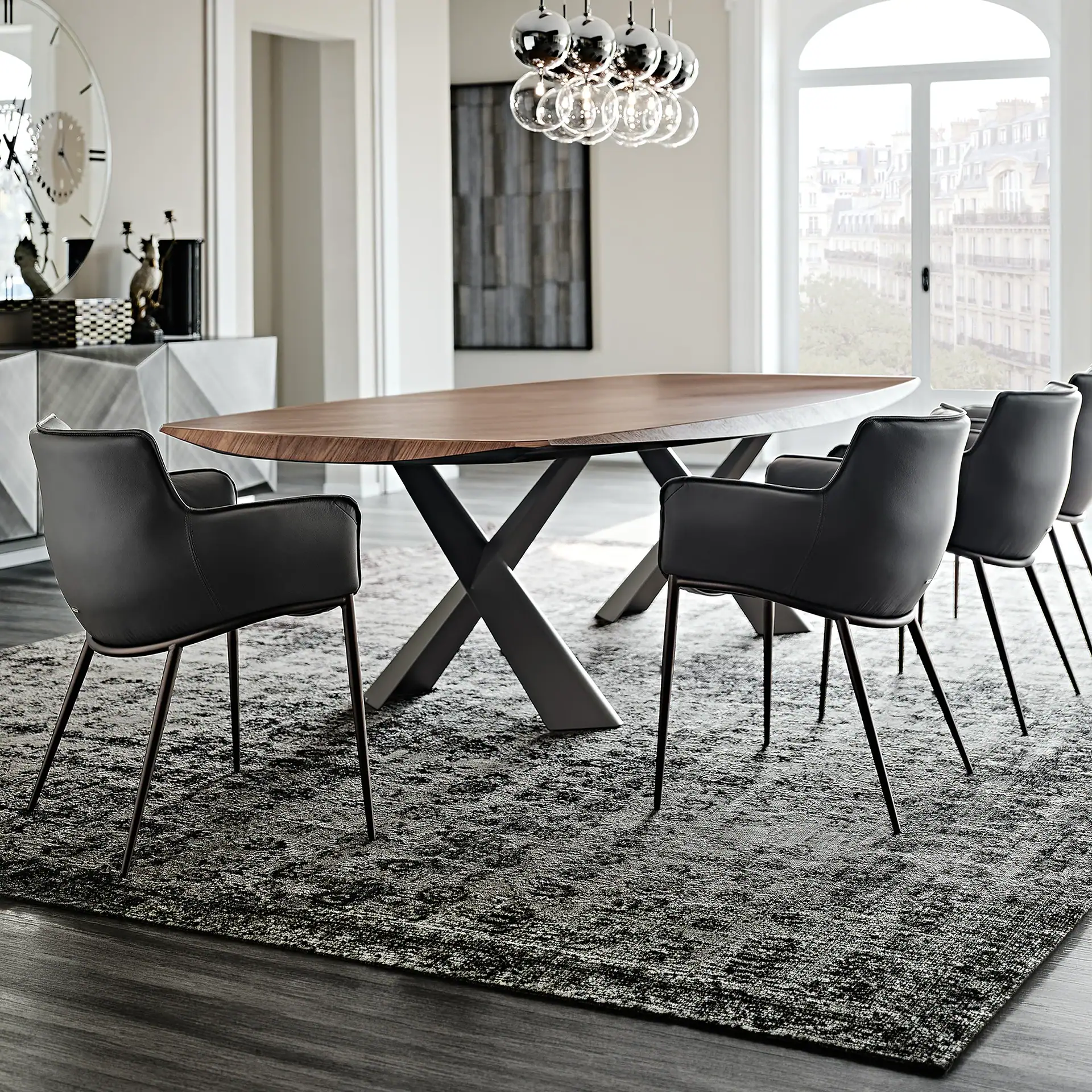 A modern dining room with an oval wooden table, black leather chairs, a grey patterned rug, and a large arched window overlooking a city.