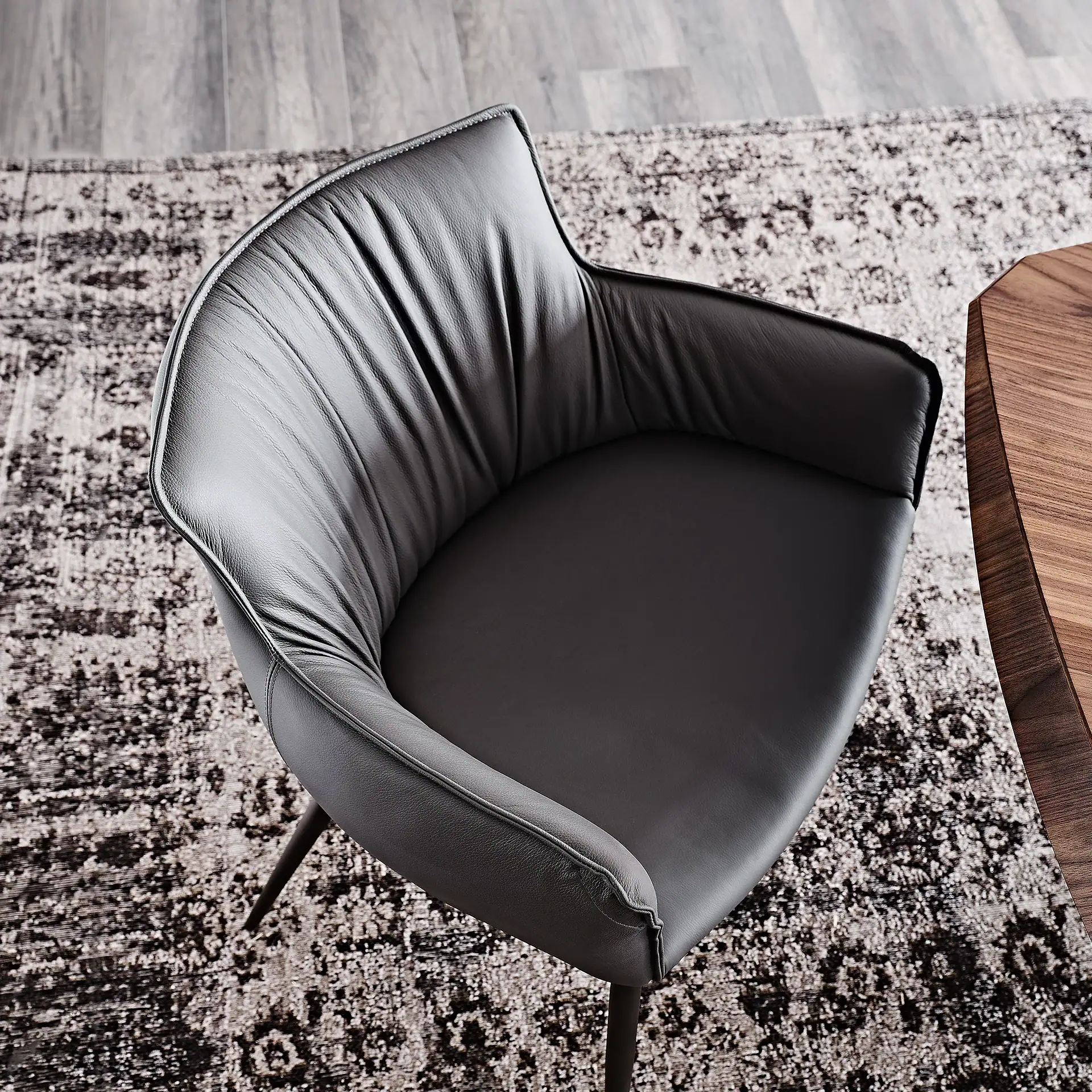A dark gray leather dining chair with curved armrests sits on a patterned rug, next to a wooden table.