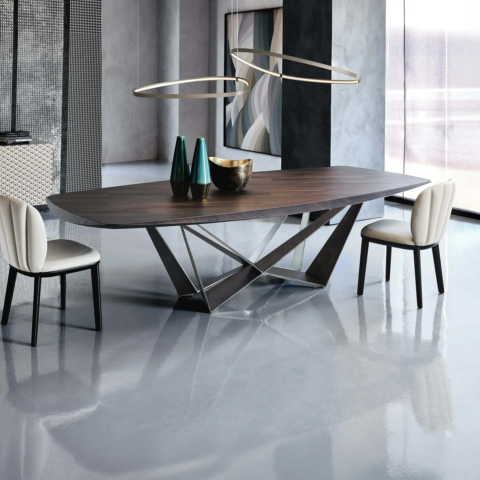 A modern dining room with a dark wood table, geometric metal base, two cream chairs, and oval pendant lights. Textured gray walls and a shiny gray floor complete the look.
