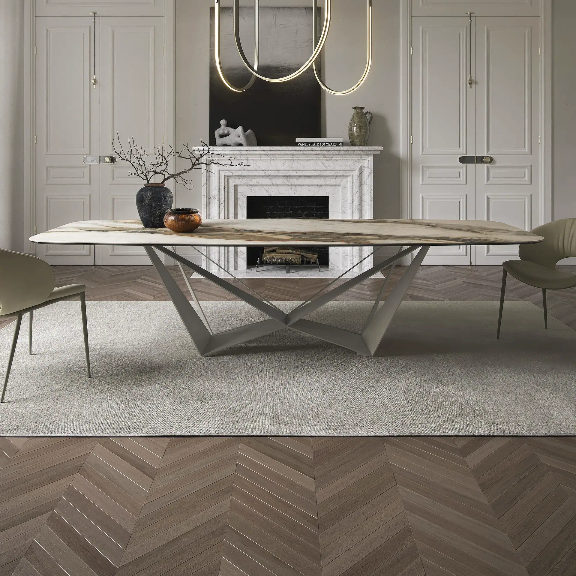 A modern dining room with a marble-top table, geometric metal base, and two beige chairs on a light rug. A white marble fireplace, two paneled doors, and a linear chandelier are in the background.