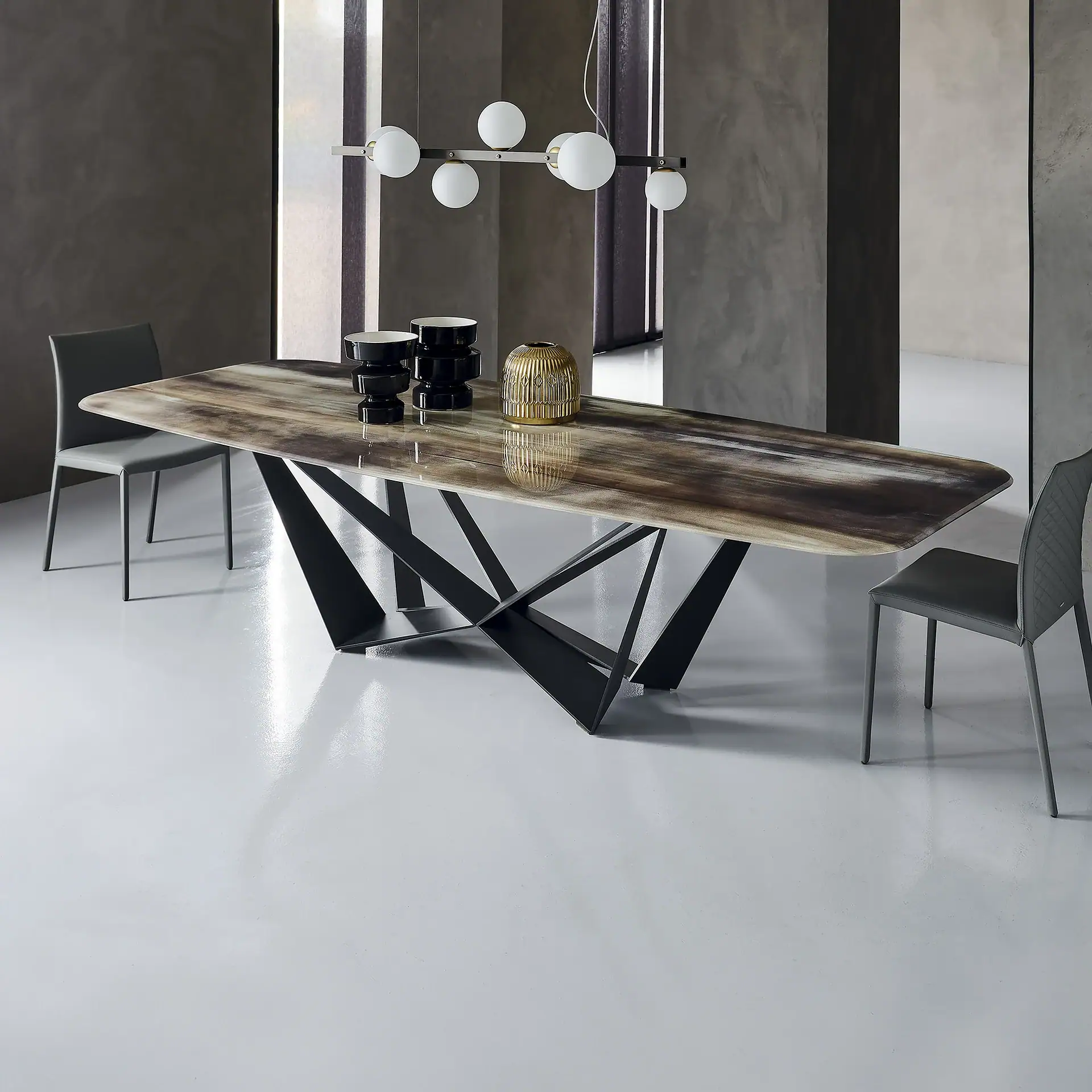 A modern dining room with a long, rectangular marble-top table on a black geometric base, flanked by two gray chairs, under a linear chandelier with white globes.