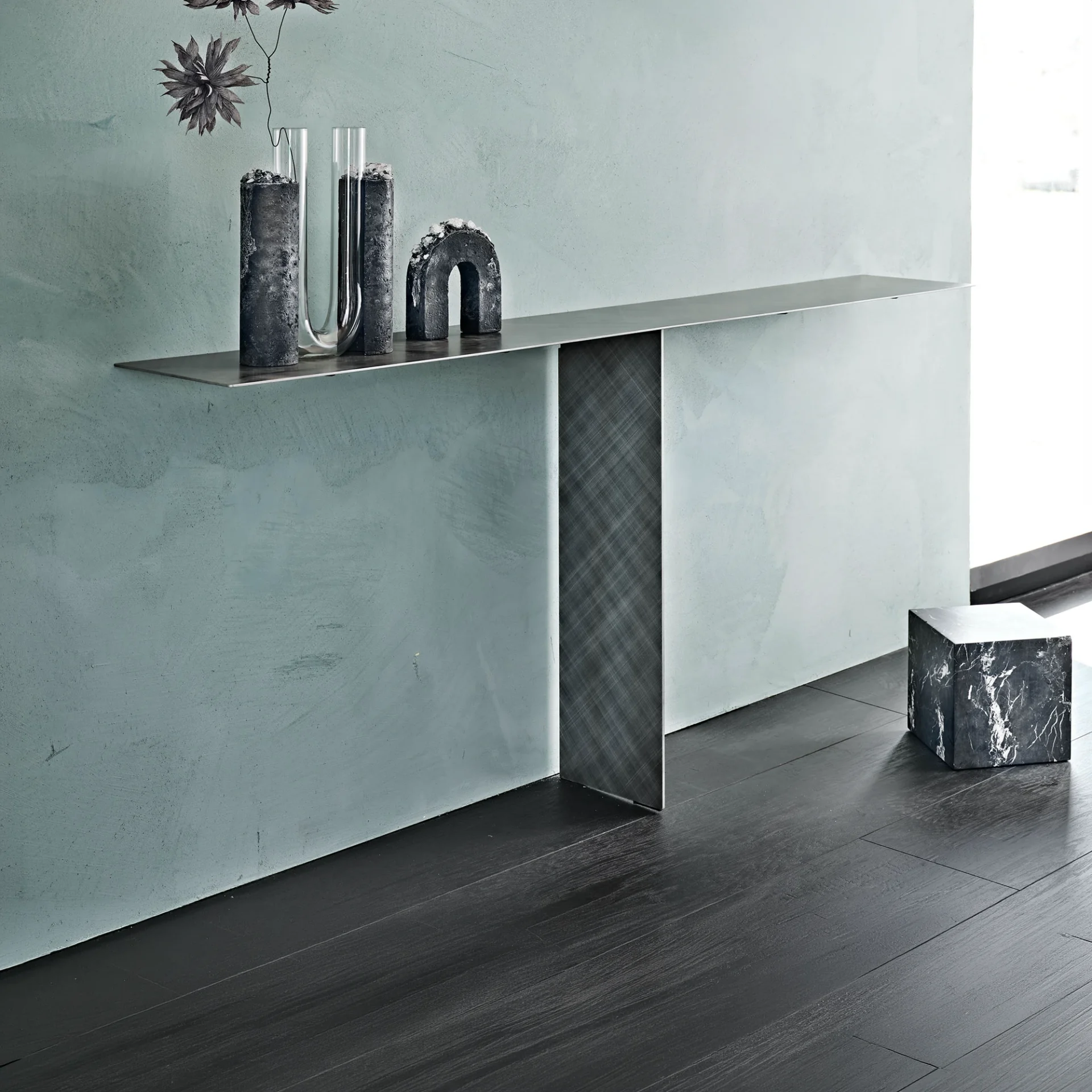 A modern console table with dark gray decor against a light blue-green wall and dark wood floor.