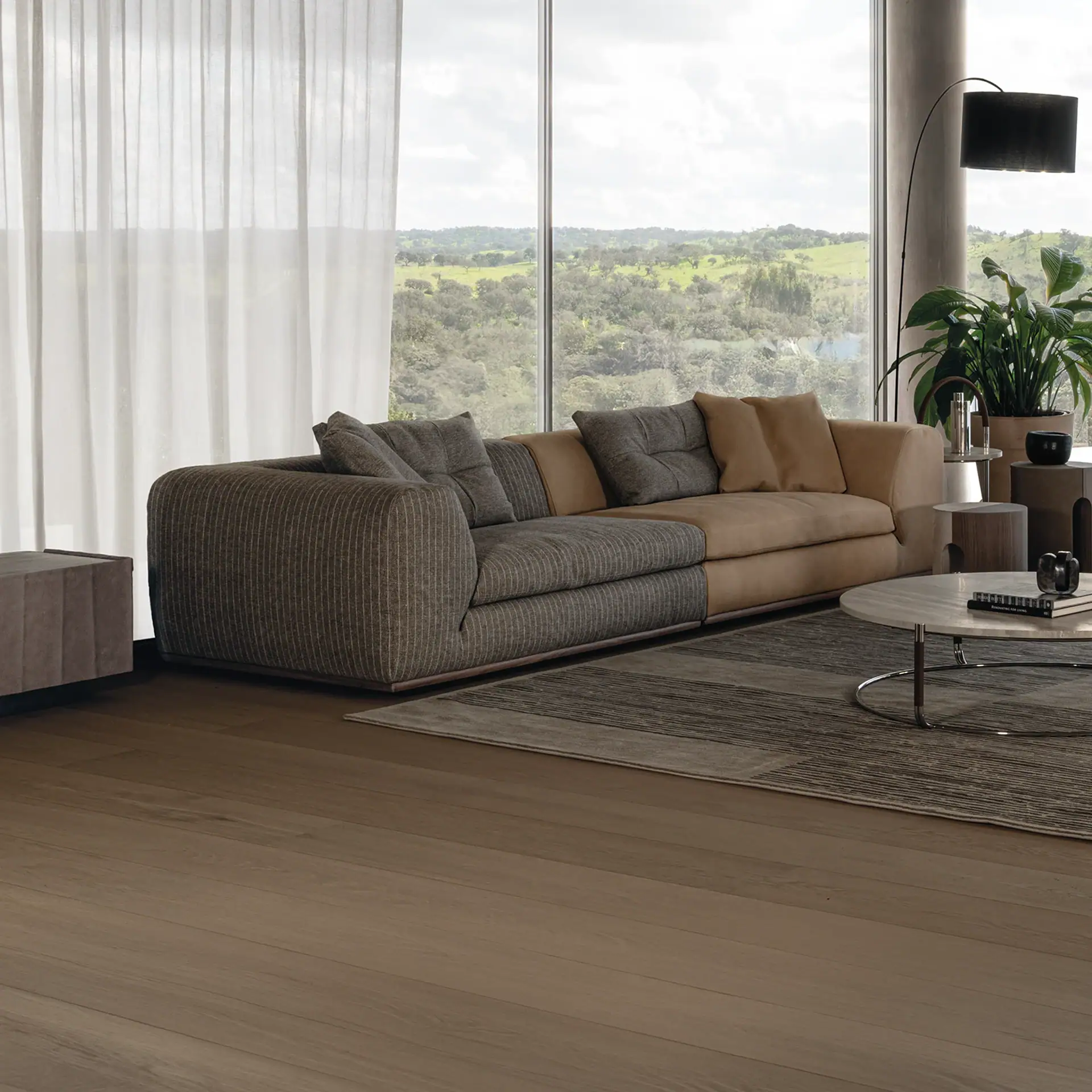 A modern living room with a two-tone sectional sofa, marble coffee table, and large windows overlooking a green, hilly landscape.