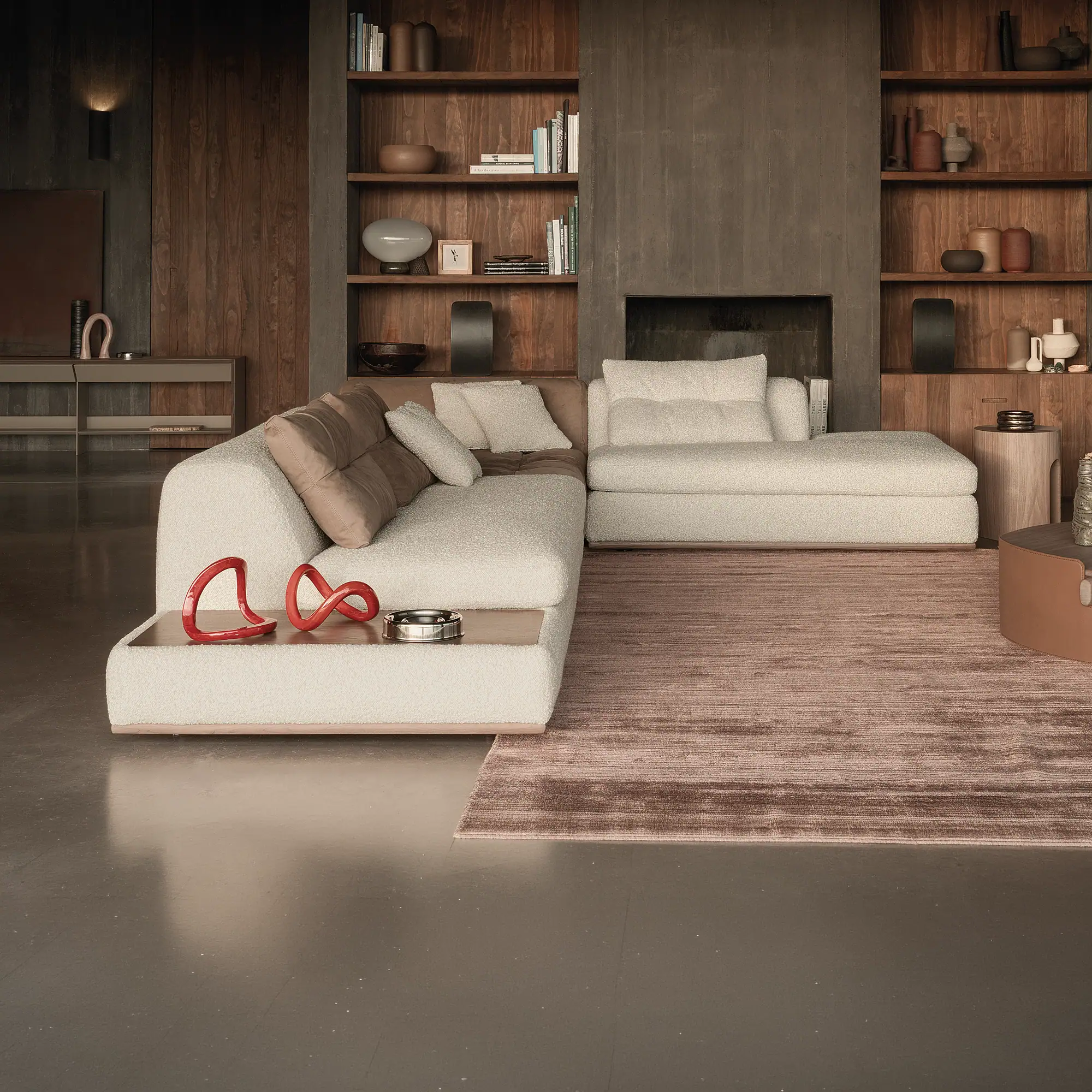 A modern living room with an L-shaped off-white bouclé sofa, a brown textured rug, and wooden built-in shelves filled with books and decorative objects.