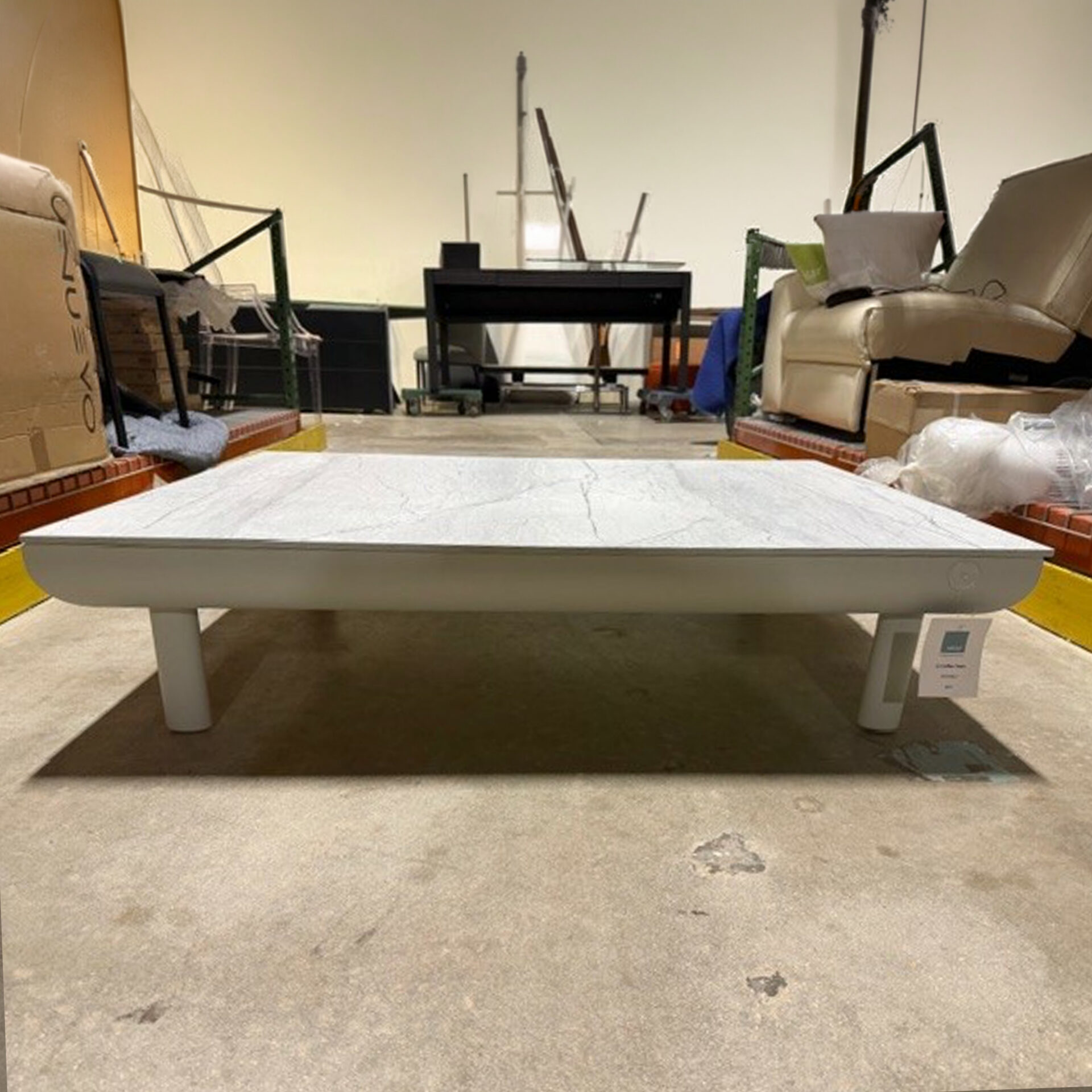 Modern rectangular coffee table with a light gray marble-patterned top and matching base, sitting on a concrete floor in a cluttered storage area.
