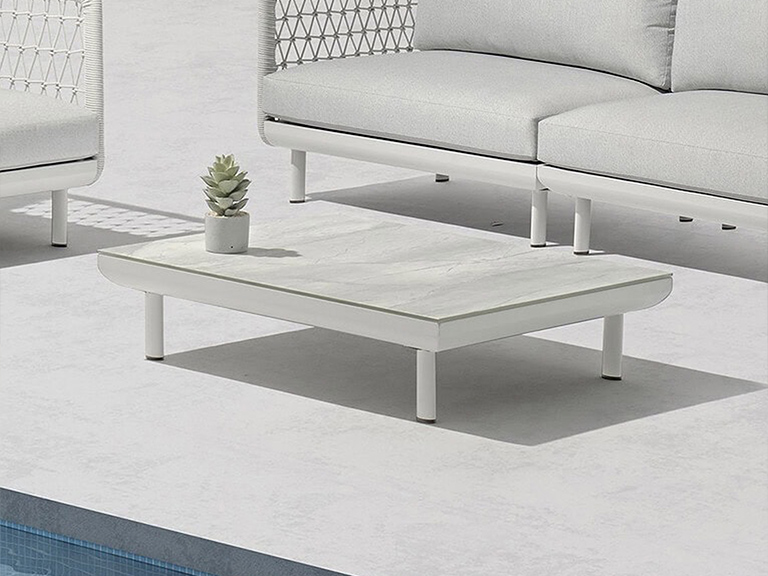A modern white outdoor coffee table with a light grey top and a succulent plant, positioned between white outdoor sofas on a light grey patio next to a swimming pool.