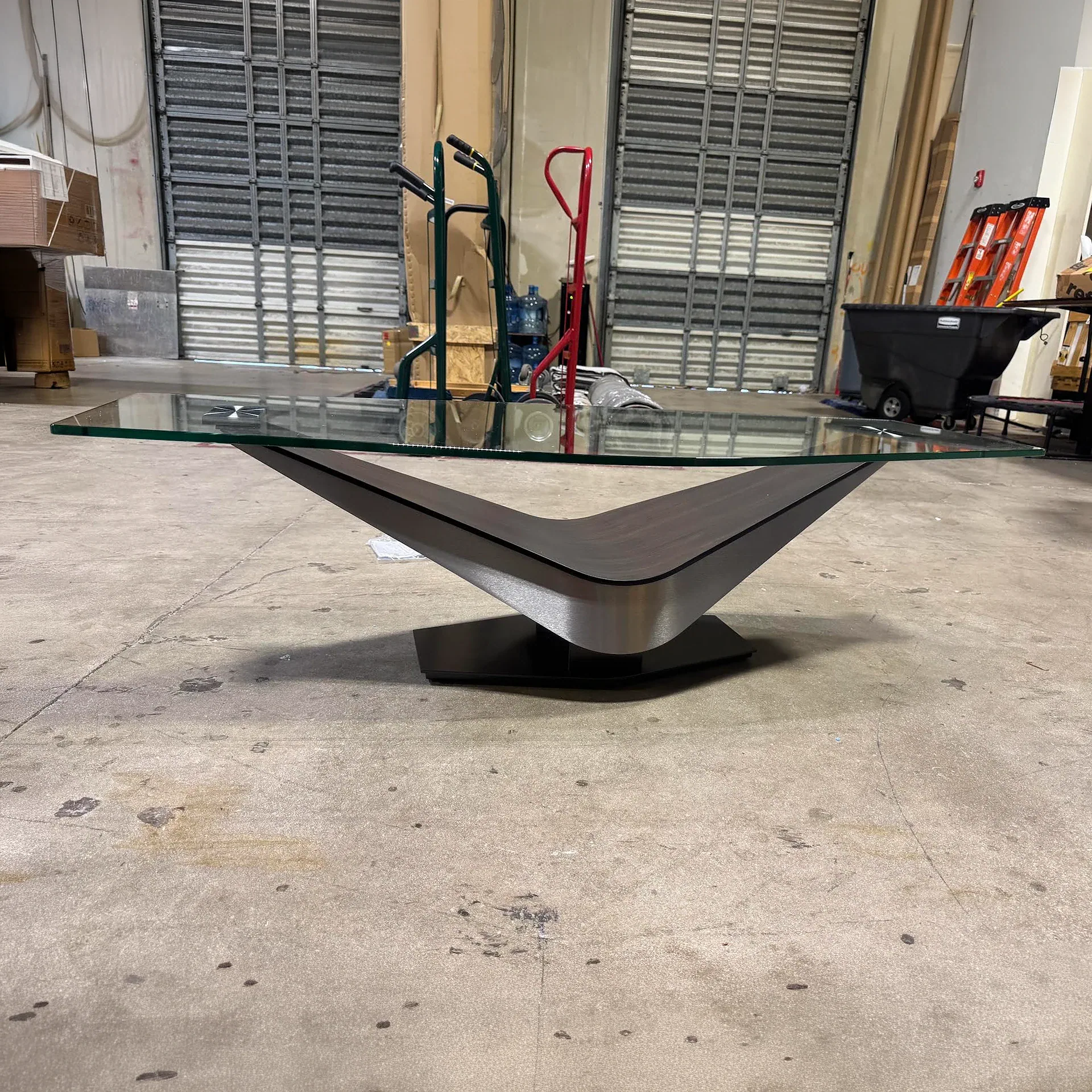 Sklar Furnishings Victor cocktail table with glass top and sculptural base in a warehouse setting.