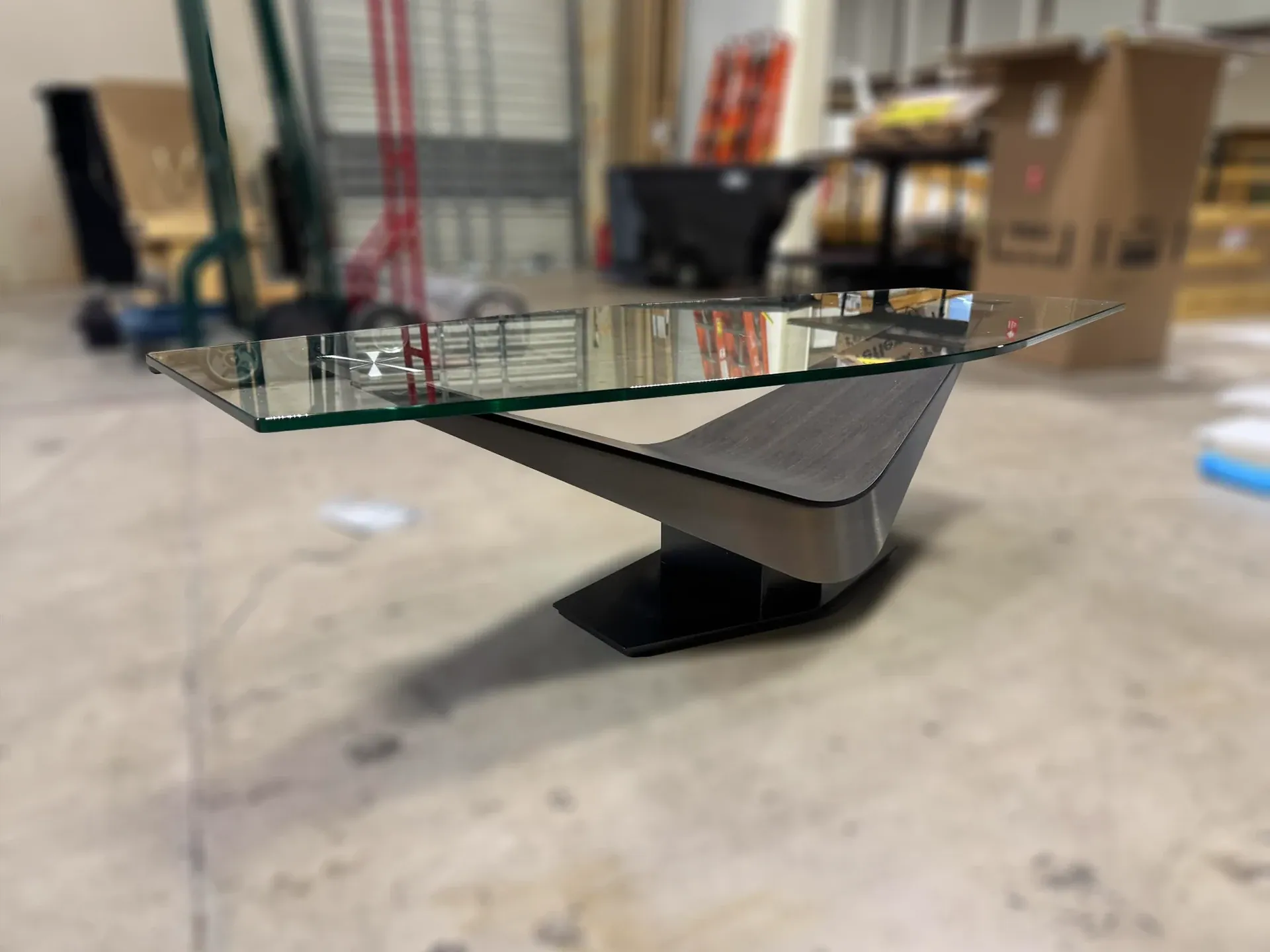 Sklar Furnishings Victor cocktail table with glass top and sculptural base in a warehouse setting.