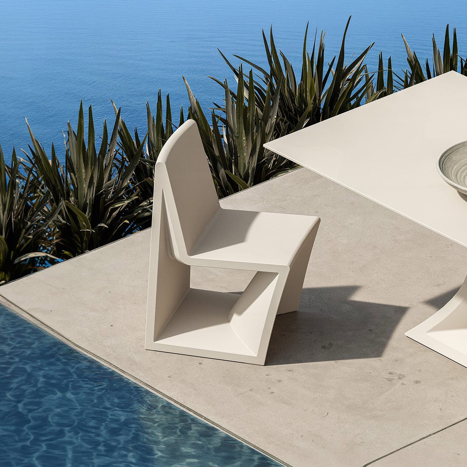 Contemporary white outdoor chair by the poolside with ocean view.