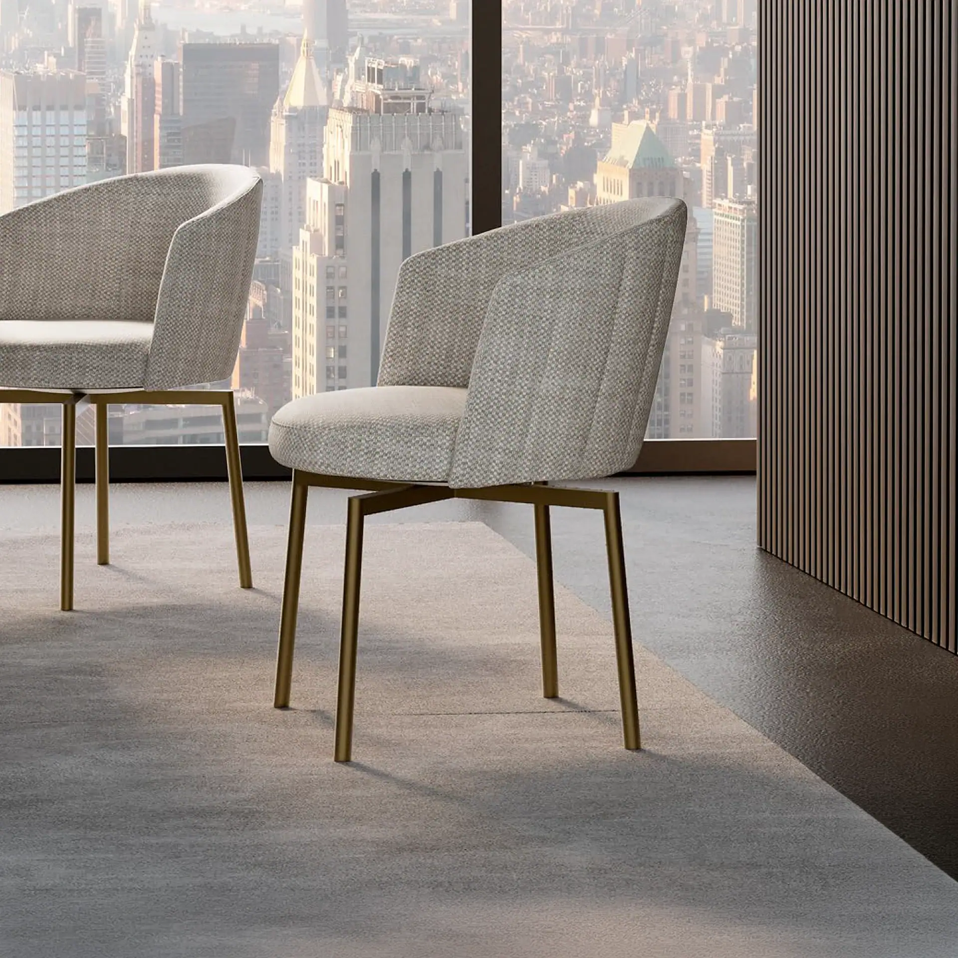 Two light gray upholstered chairs with golden metal legs in a modern room overlooking a city skyline through a large window.