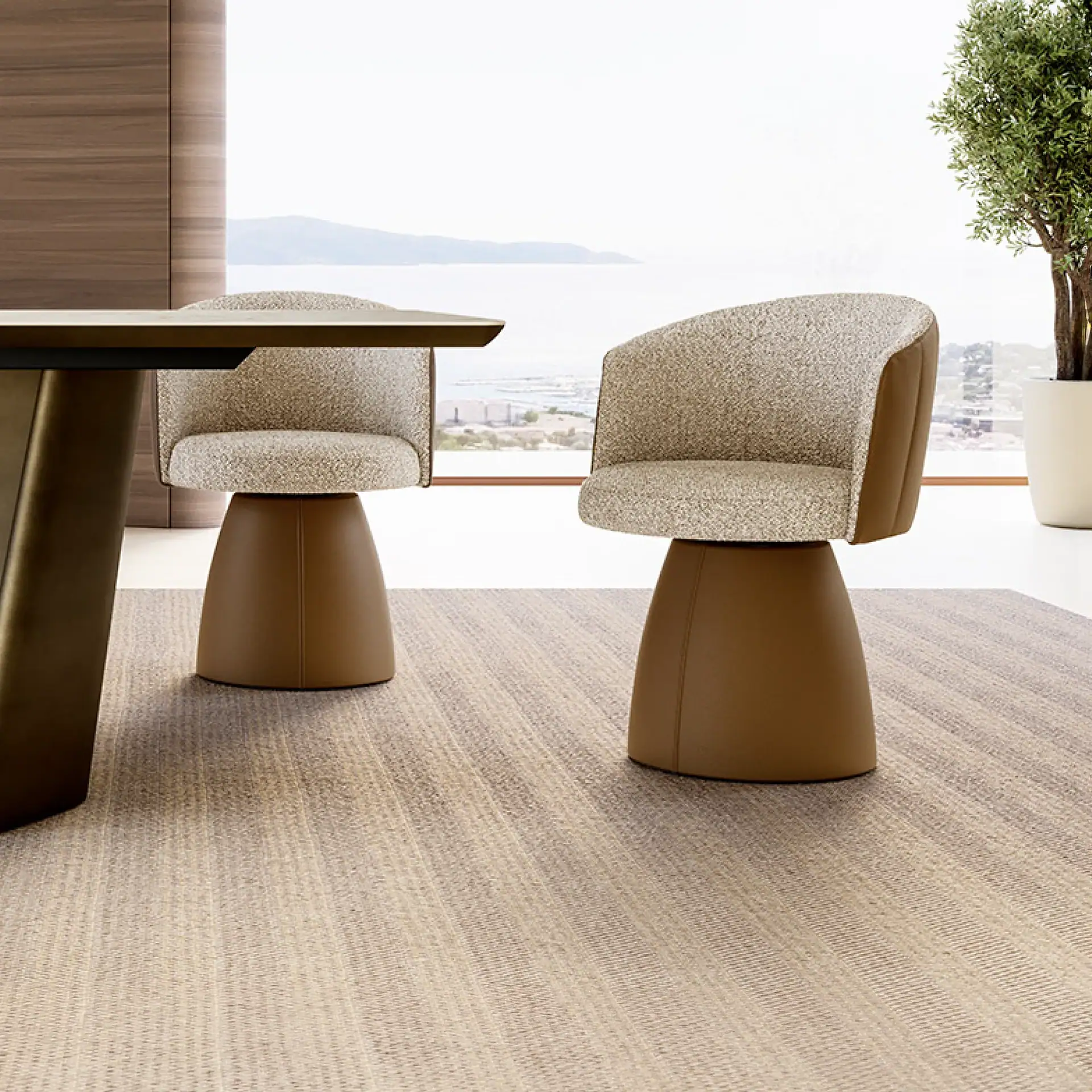Two modern dining chairs with cream textured upholstery and tan leather bases sit on a striped rug in front of a large window overlooking a sea and distant mountains.