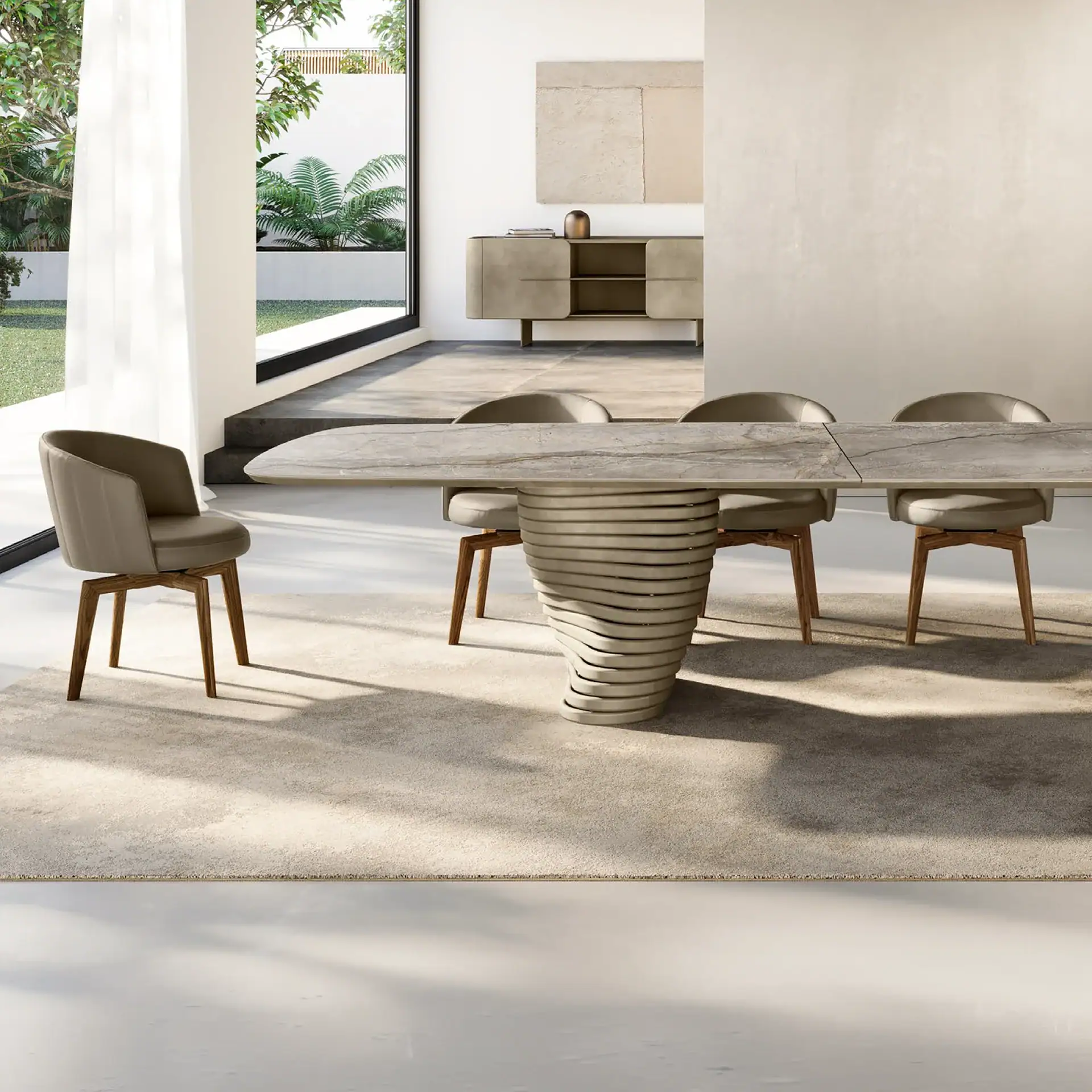 A modern dining room with a long, light gray table on a spiral base, surrounded by five upholstered chairs on a beige rug. Large windows overlook a green garden, and a neutral-toned sideboard with abstract art is in the background.