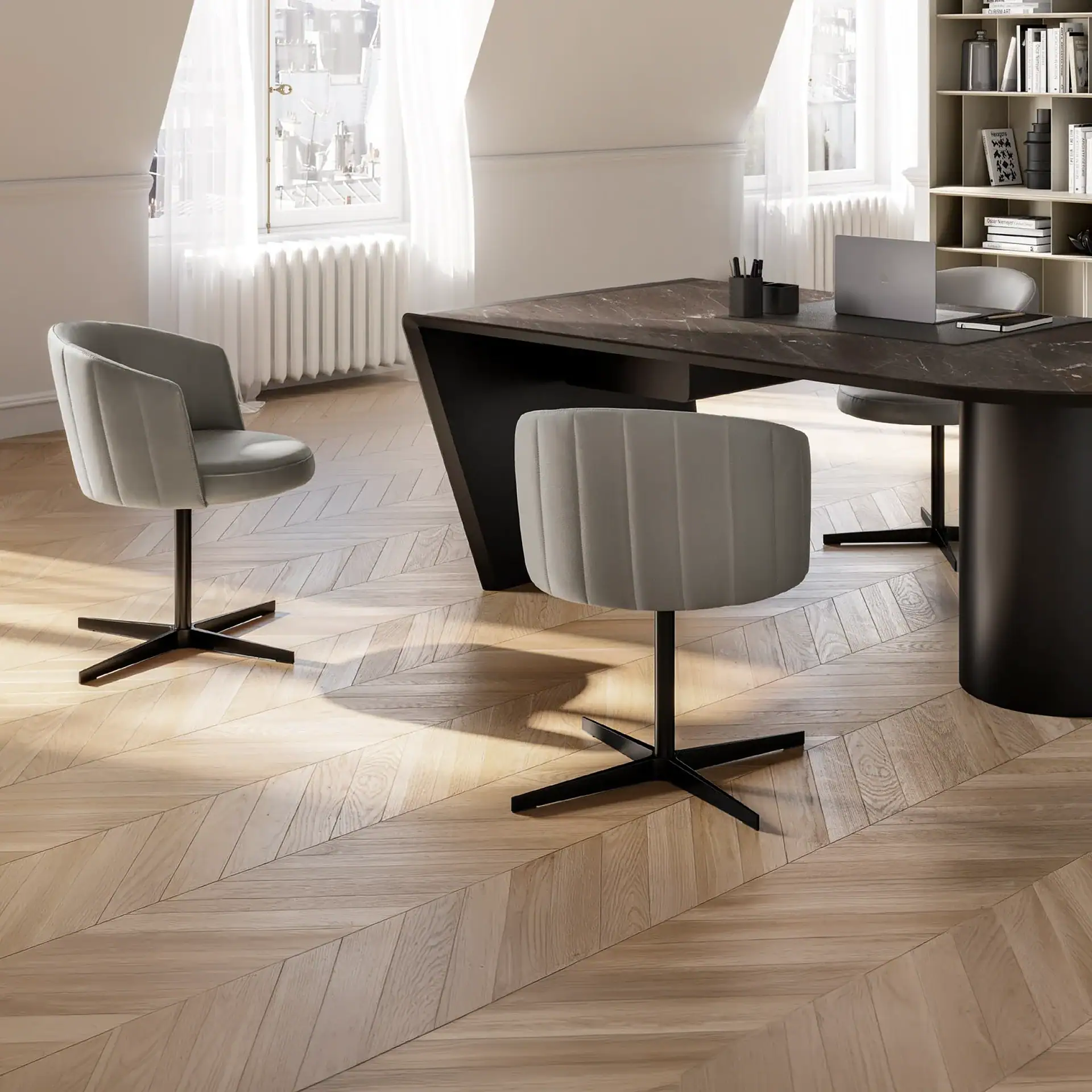 A modern home office with a dark marble desk, two grey upholstered chairs, a laptop, and a bookshelf, set against light walls and herringbone wood floors.