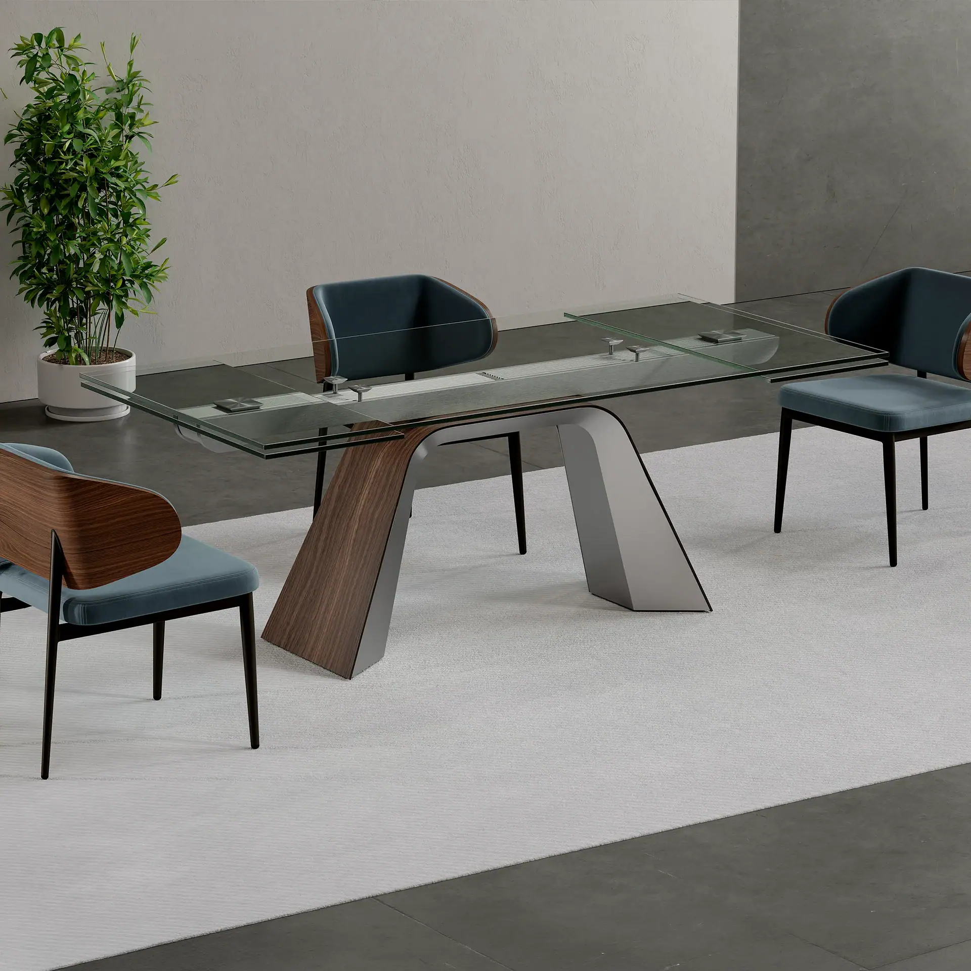 A modern dining room with a glass-top extendable table, a unique wood and metal base, and three teal upholstered chairs. A tall green plant is in the corner.