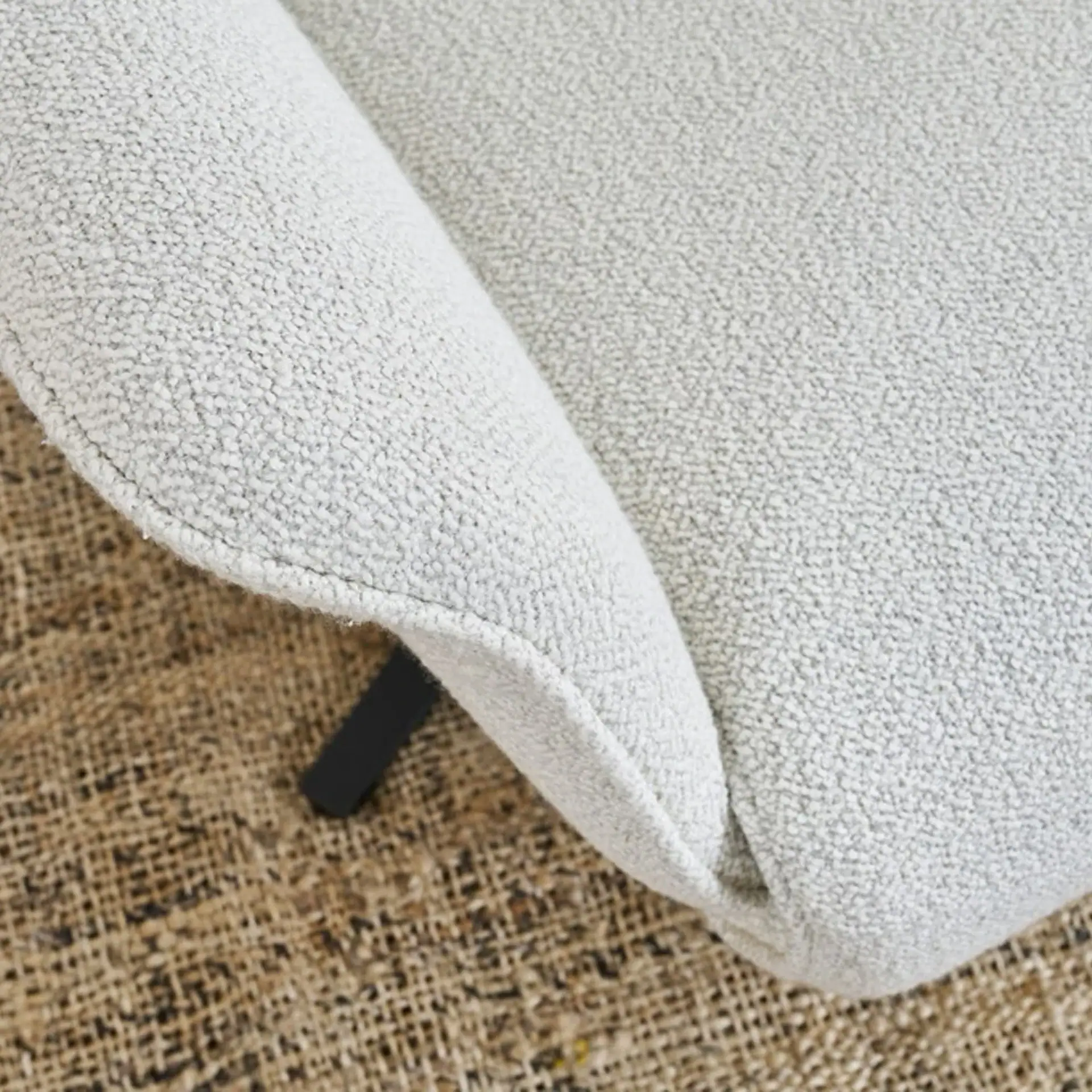 Close-up of light gray textured upholstery on a brown woven rug, with a dark furniture leg visible.