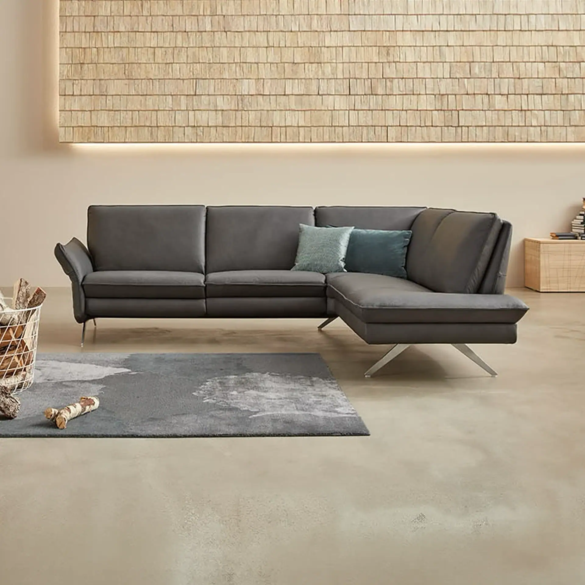 A modern living room with a dark gray L-shaped sectional sofa, a wooden shingle wall panel with backlighting, and a gray rug on a concrete floor.
