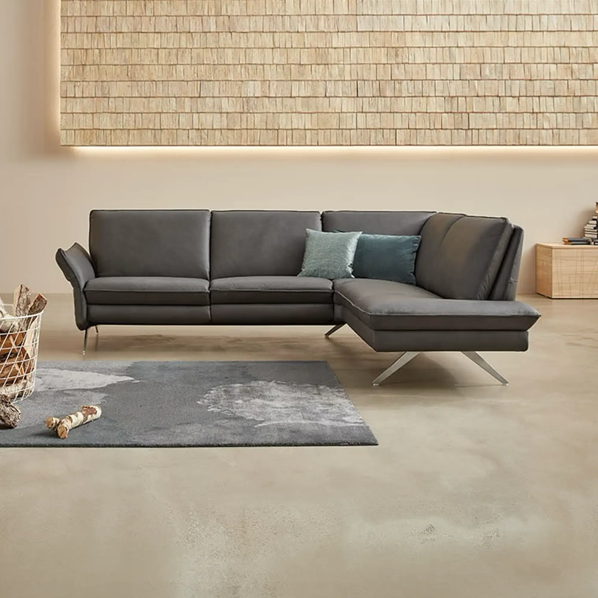A modern living room with a dark gray L-shaped sectional sofa, a wooden shingle wall panel with backlighting, and a gray rug on a concrete floor.