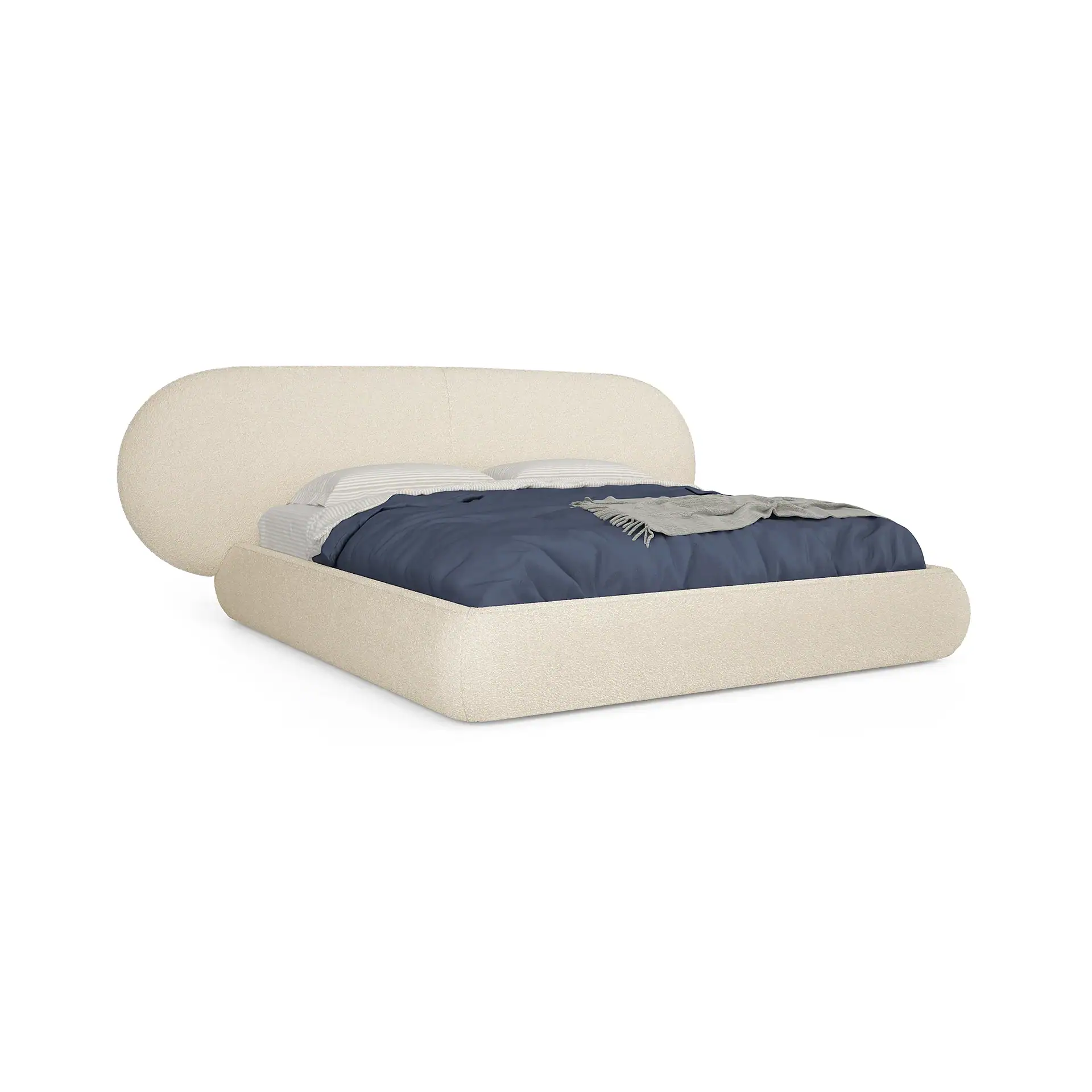 A modern, light beige upholstered bed with a rounded headboard, navy duvet, and gray throw blanket on a white background.