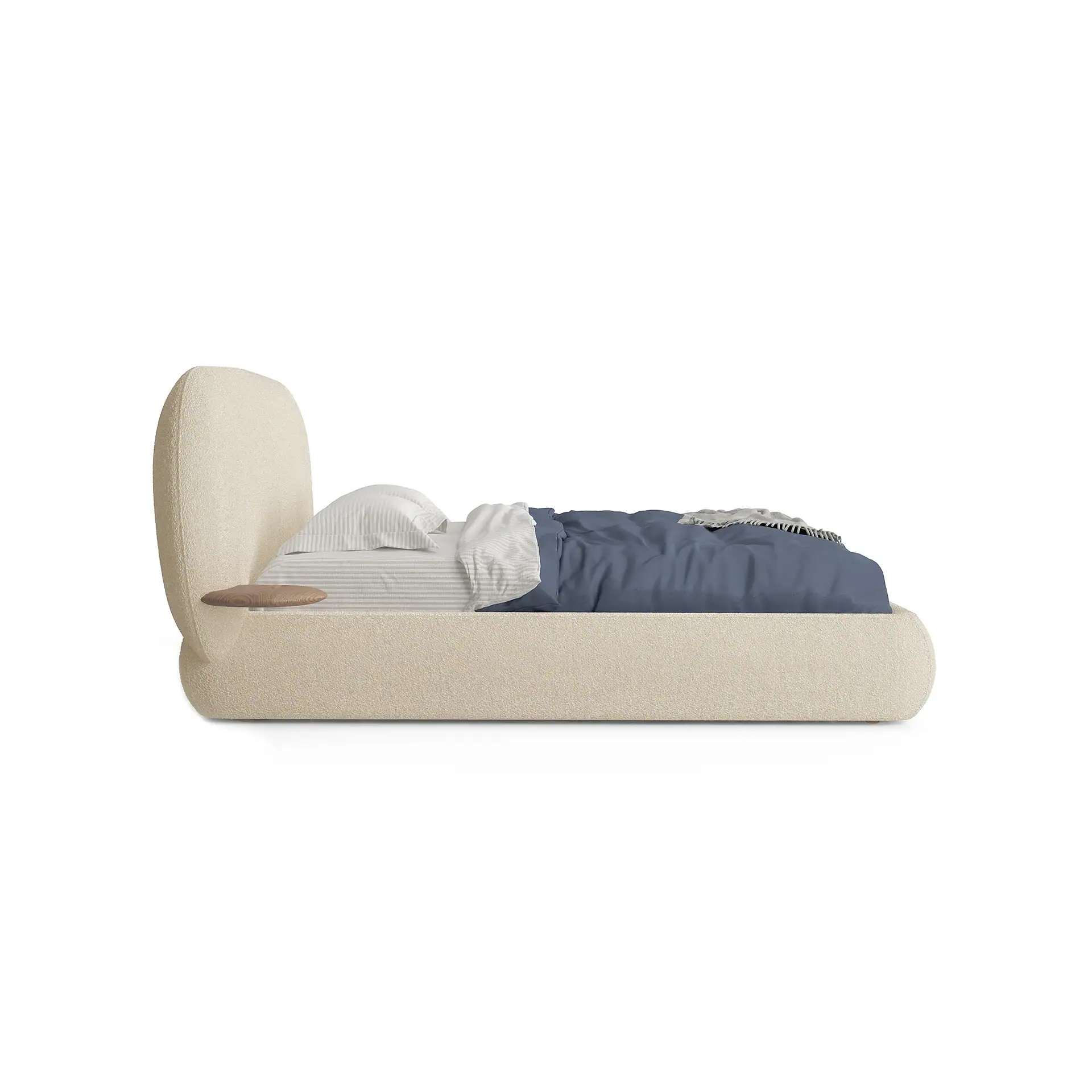 A modern bed with a beige upholstered frame, curved headboard, and an integrated wooden side shelf. It is dressed with striped sheets, a white pillow, a blue duvet, and a grey throw blanket.