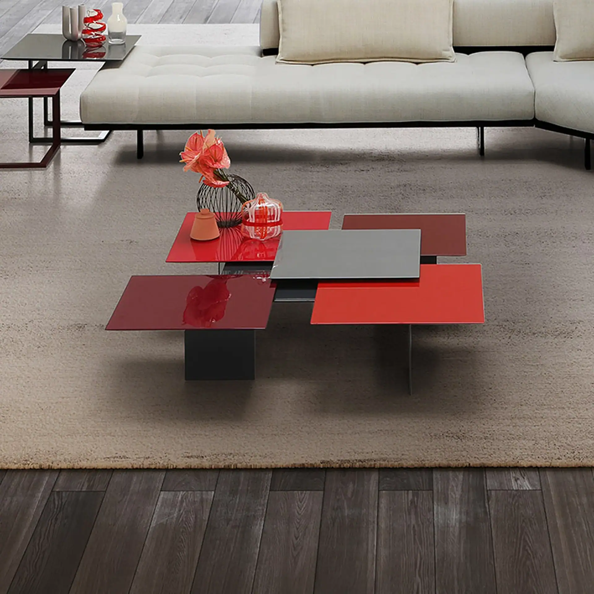 Modern living room with a multi-level red and gray coffee table, a beige sectional sofa, and a light brown rug on a wooden floor.