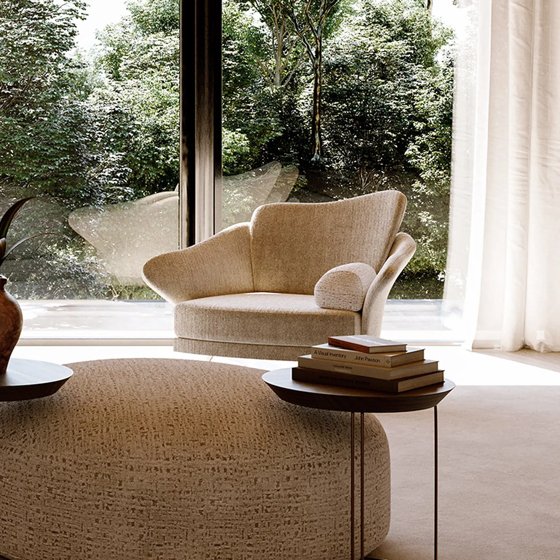 A modern living room with a beige armchair and ottoman facing a large window overlooking green trees. A side table holds books.