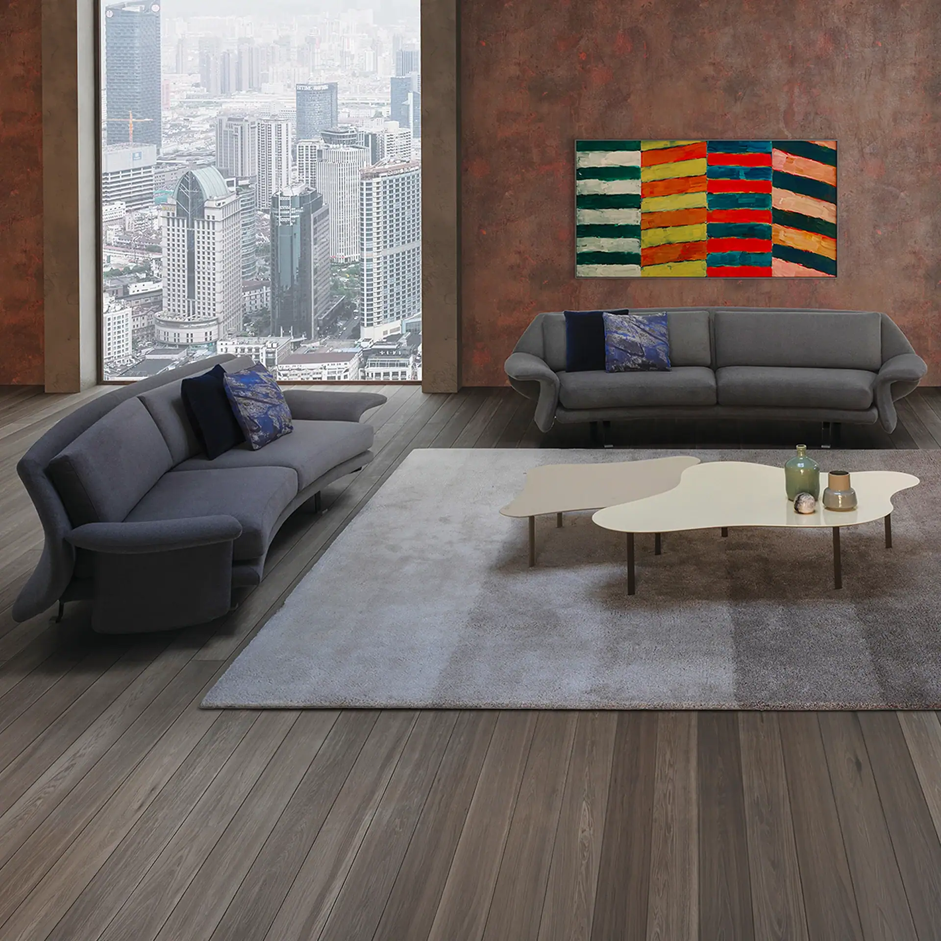 A modern living room with two gray sofas, a large abstract painting, and two organic-shaped coffee tables. A large window offers a panoramic view of a hazy city skyline with skyscrapers.