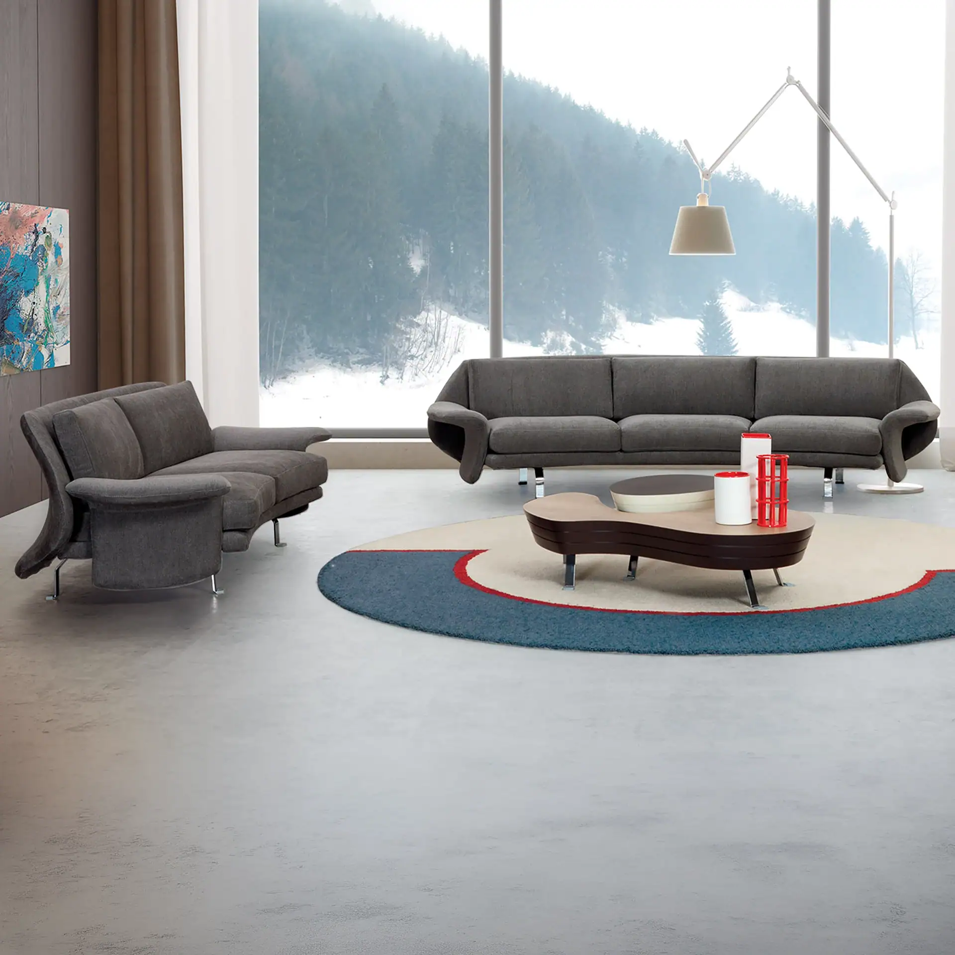 A modern living room with dark grey sofas, a unique coffee table on a circular rug, and large windows overlooking a snowy mountain landscape.