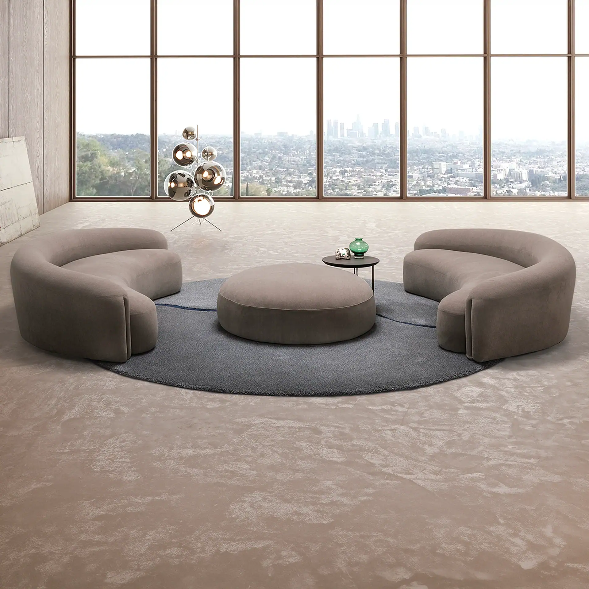 A modern living room with two curved sofas, a round ottoman, and a side table on a circular rug, facing large windows with a city skyline view.