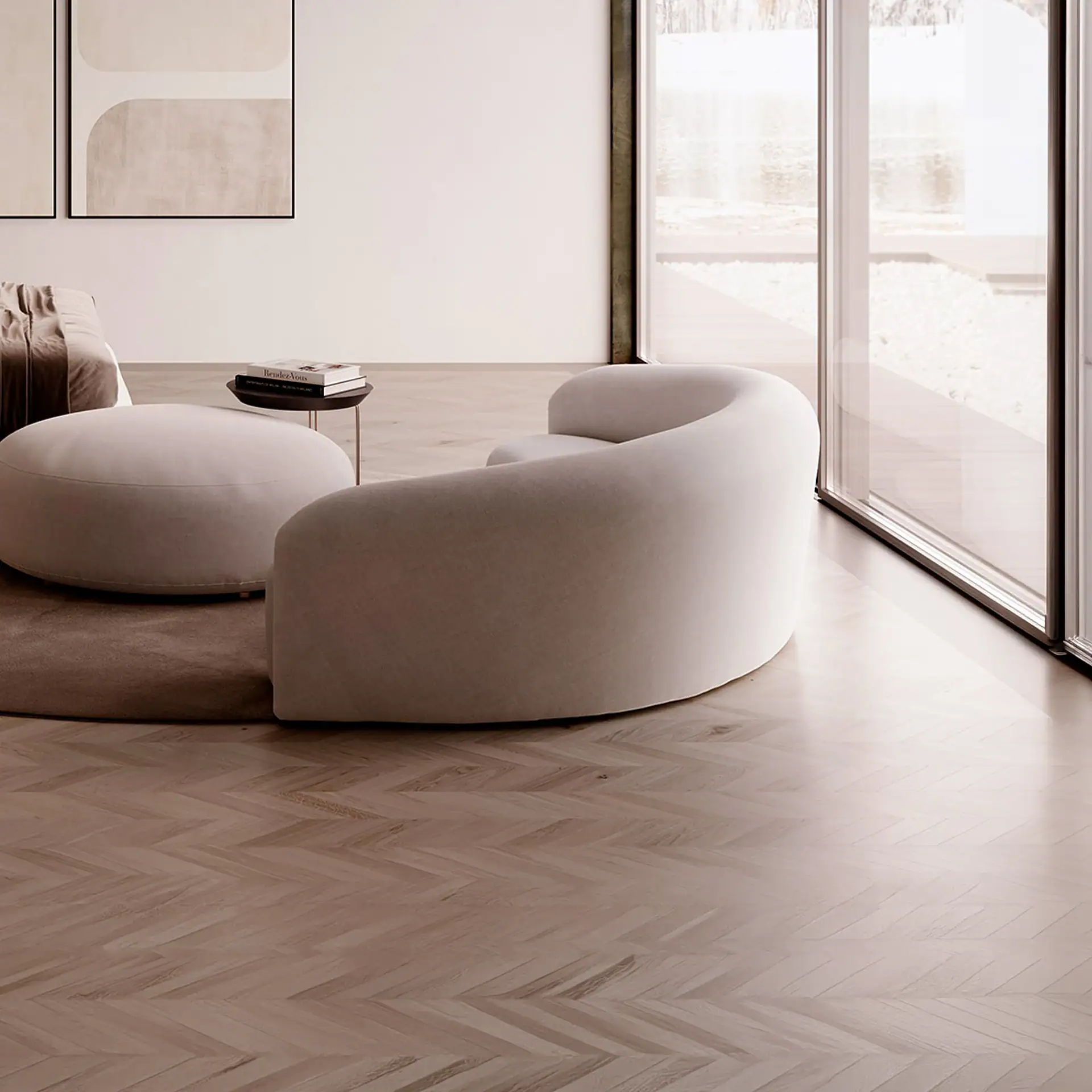 A modern living room with a curved light beige sofa, matching ottoman, and a small side table on a dark rug. The room has light herringbone wood floors, white walls with abstract art, and a large window overlooking an outdoor area with light pebbles.