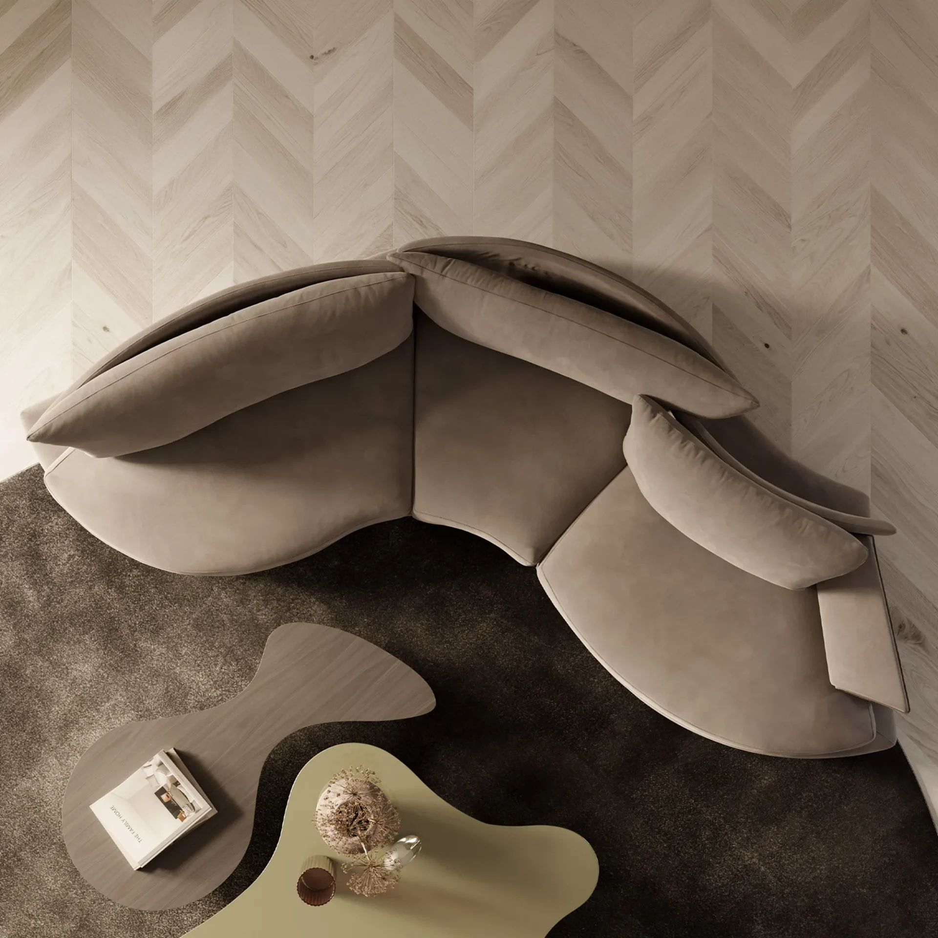 Overhead view of a modern living room with a curved taupe sofa, dark rug, and two irregularly shaped coffee tables on a herringbone wood floor.