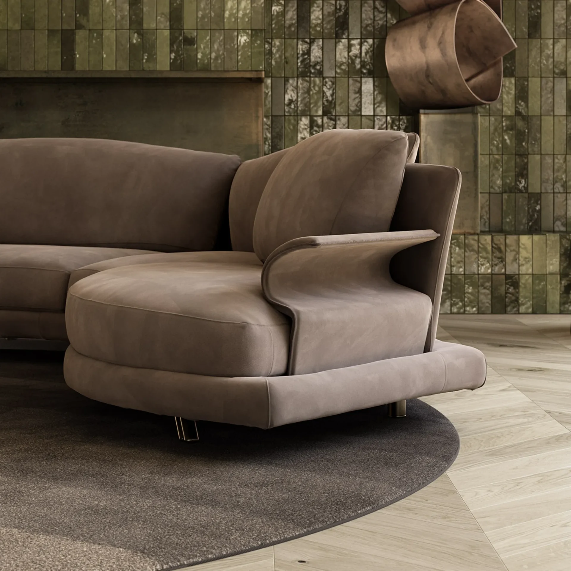 A modern taupe sectional sofa with a curved armrest sits on a gray rug and light wood floor, in front of a dark green tiled wall with a bronze sculpture.