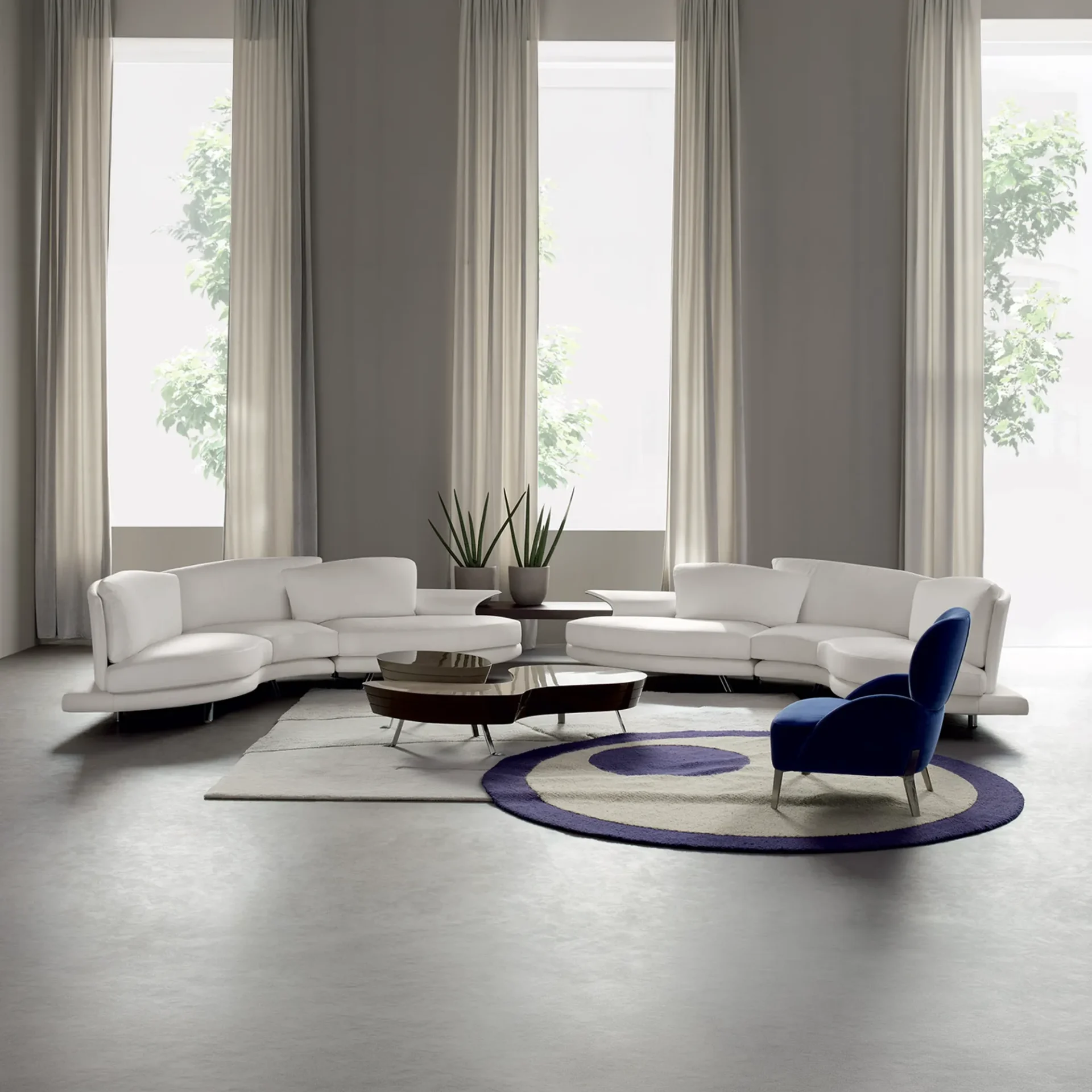 A modern living room with two curved white sofas, a blue armchair, and two coffee tables on a light gray rug. Tall windows with sheer curtains reveal green trees outside.