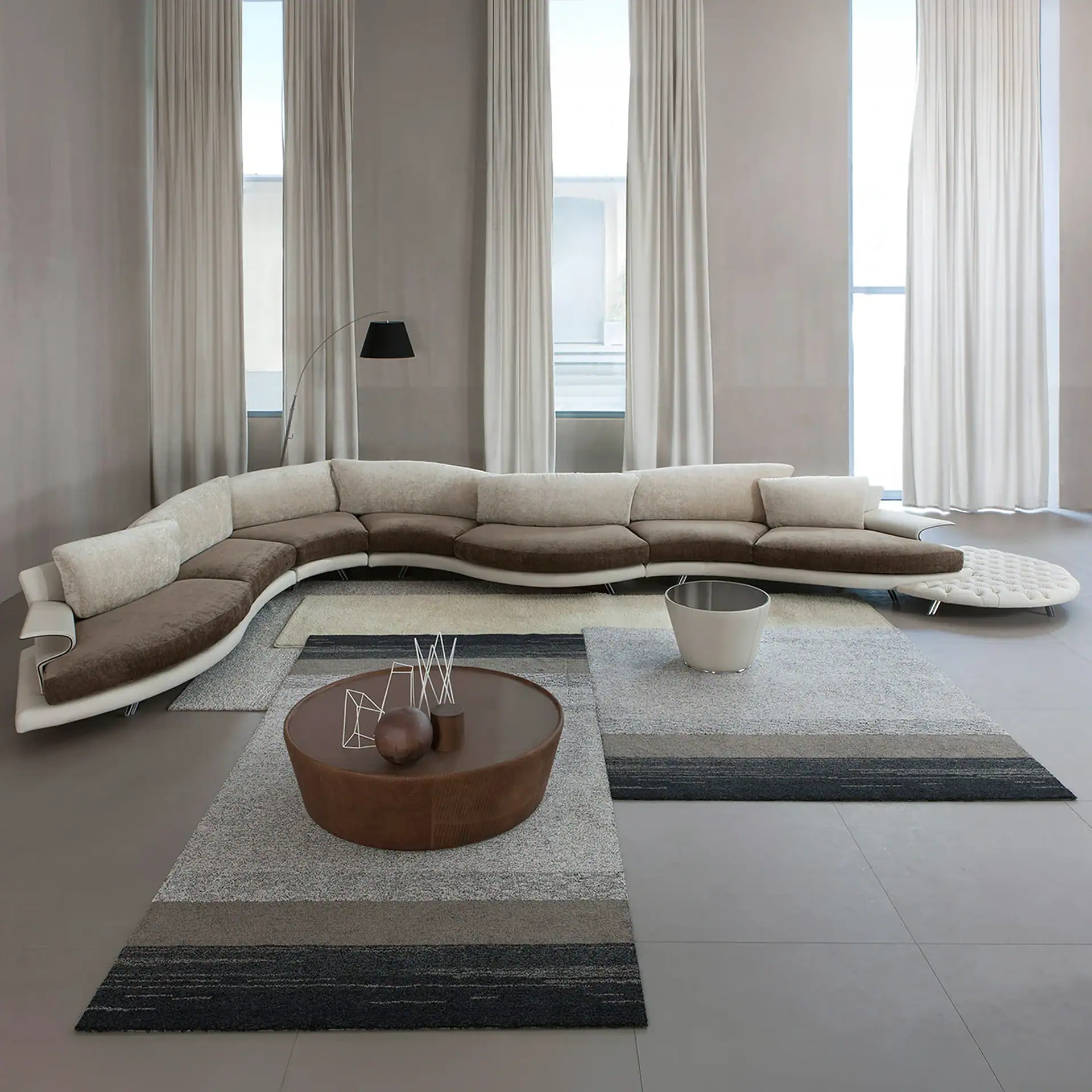 A modern living room with a Super Roy Modular Curved Sofa, layered striped rugs, a round coffee table, and tall windows with light curtains.