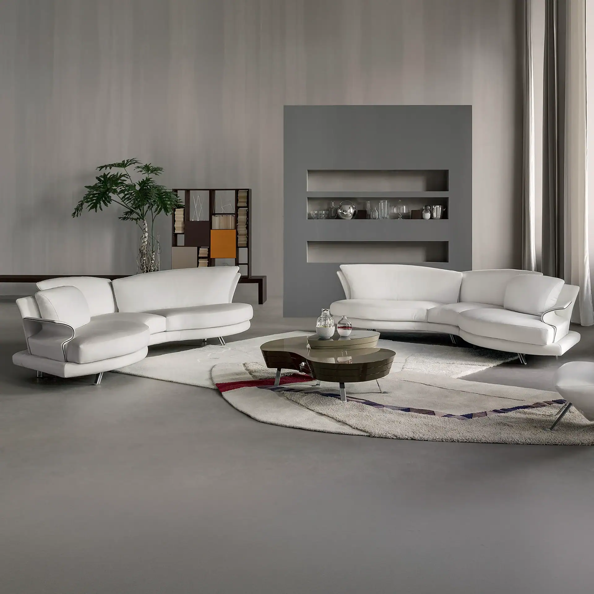 A modern living room with two Super Roy Modular Curved Sofas, a multi-tiered coffee table, and a patterned rug on a gray floor.