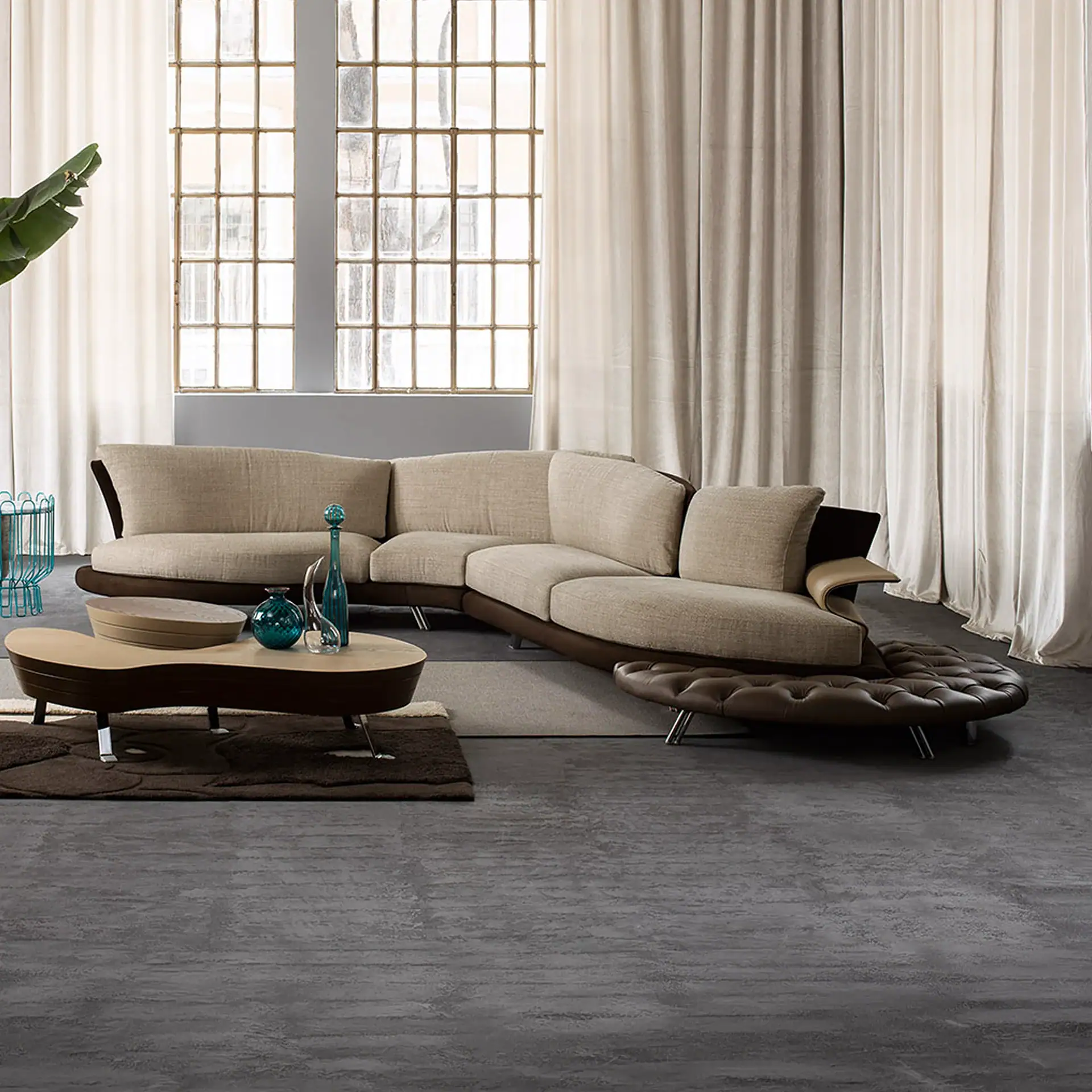 A modern living room with a Super Roy Modular Curved Sofa, a curved wooden coffee table with teal decor, and a large industrial window with light beige curtains.